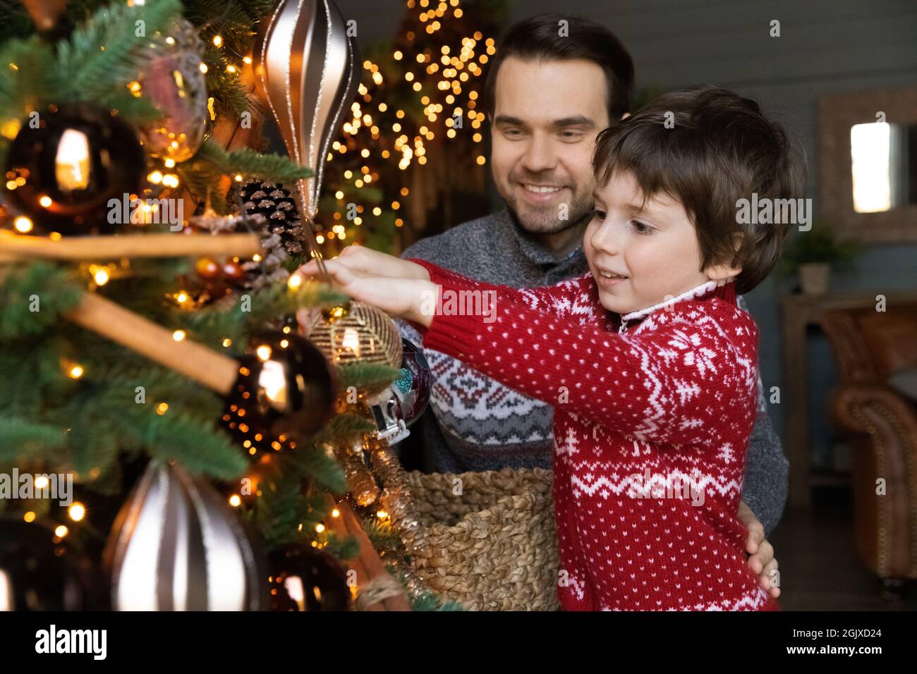 Joyeux jeune homme aidant petit enfant fils décorant l'arbre de noël. Banque D'Images