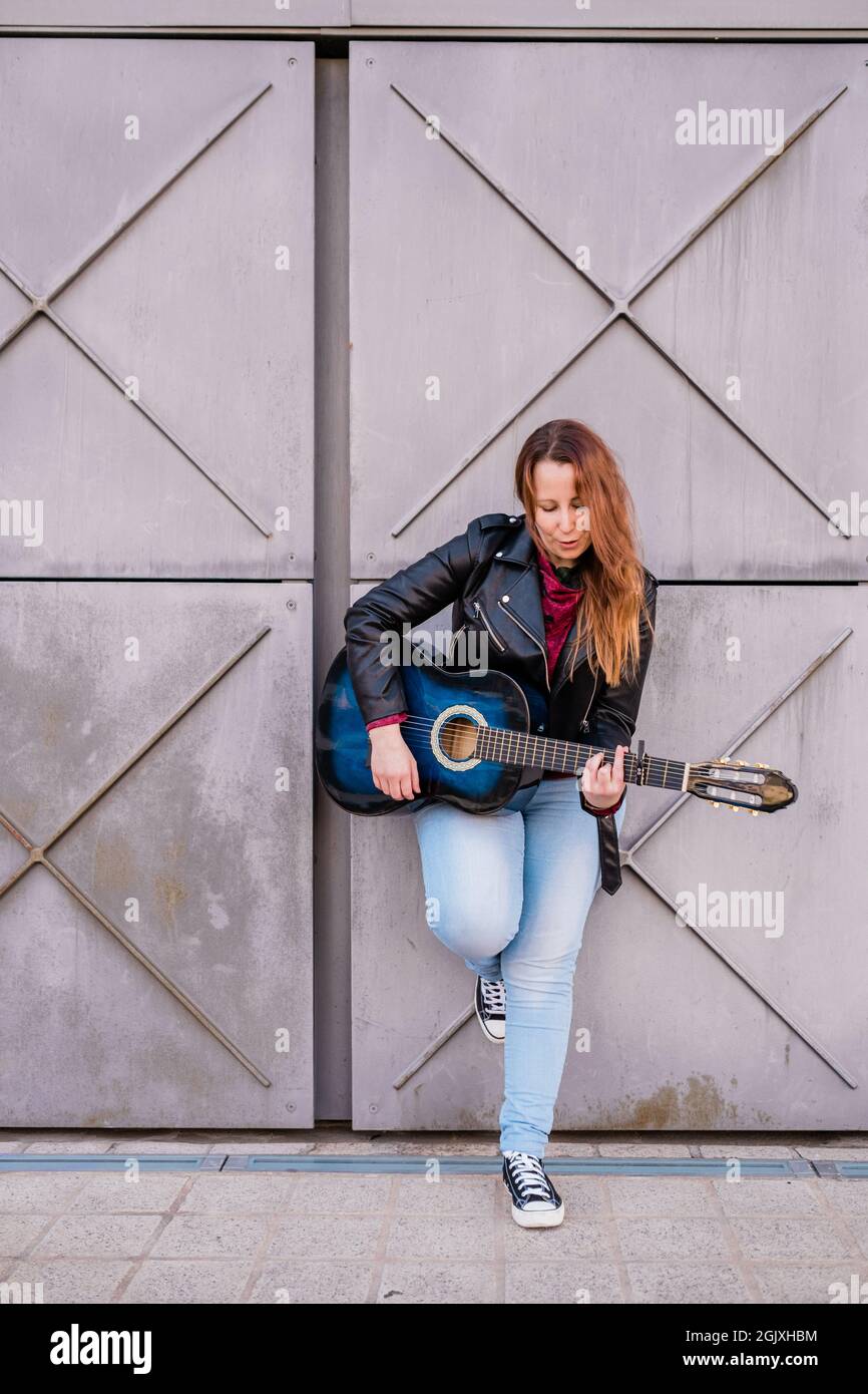 Musicien de rue jouant de la guitare acoustique. Jeune femme portant une veste à l'extérieur Banque D'Images