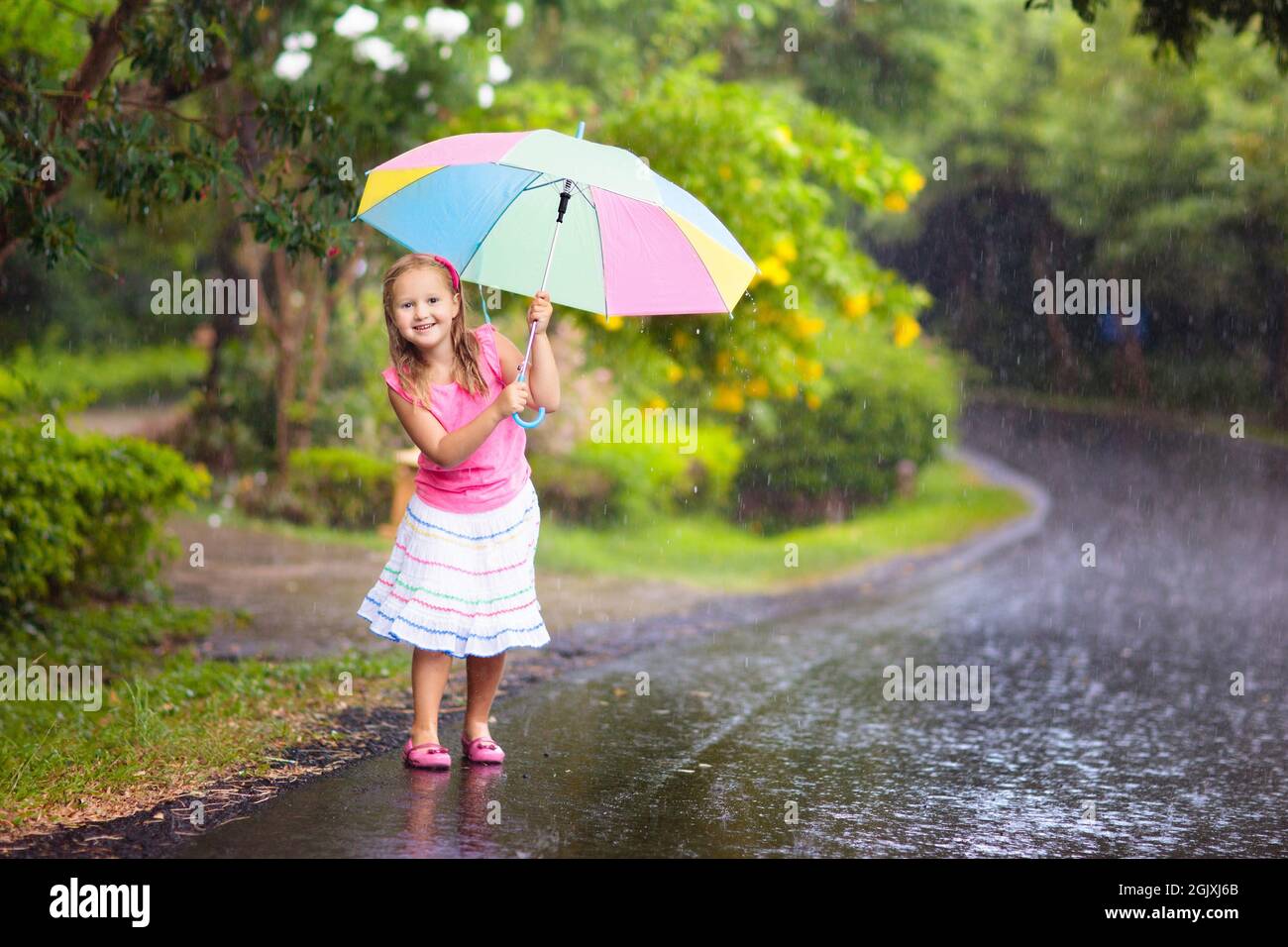 Kid jouer dehors sous la pluie. Les enfants jouent dehors avec parapluie en cas de pluie. Petite fille pris en premier ressort d'une douche. Kids Fun en plein air par rainy Banque D'Images