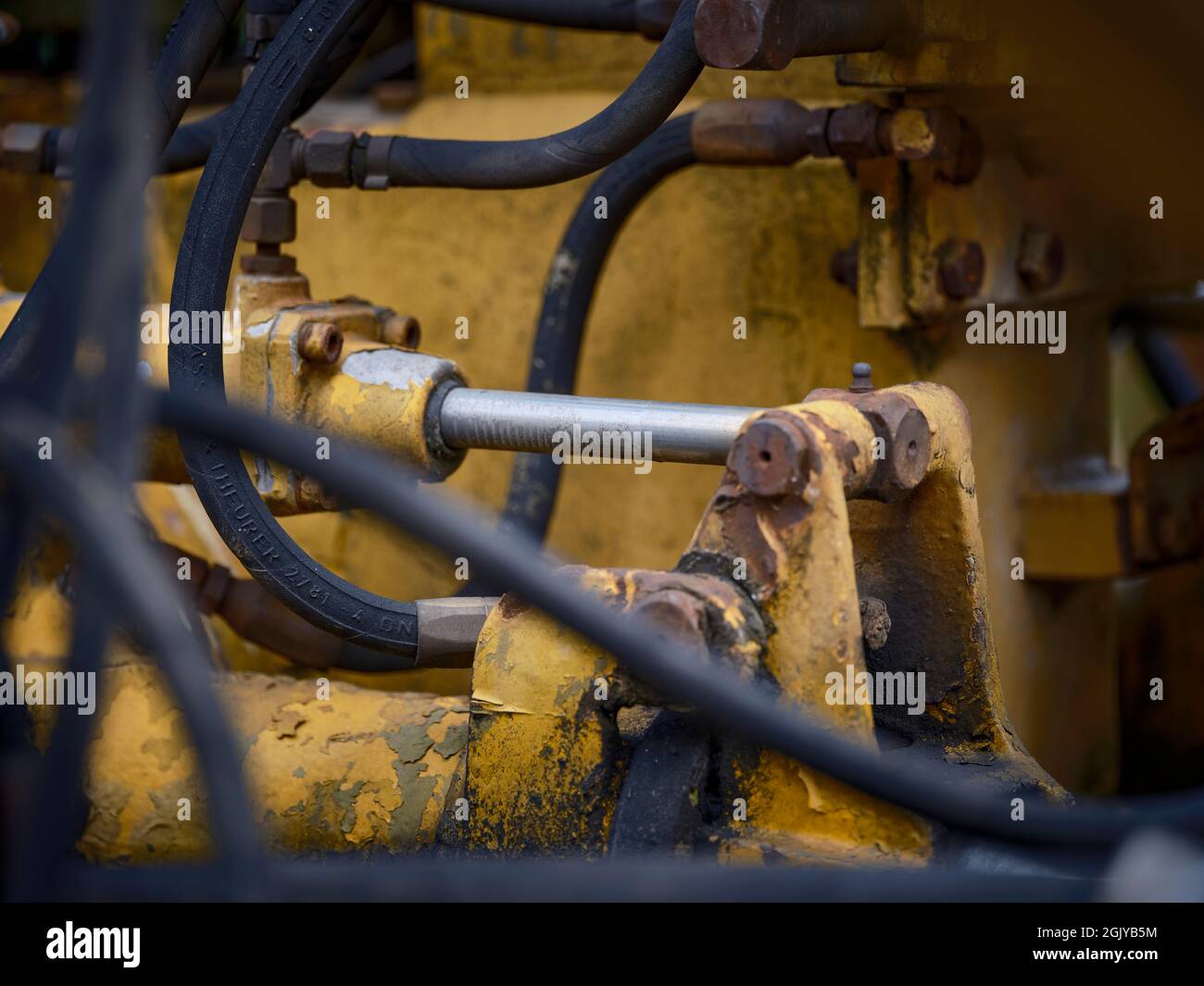 Gros plan d'un piston hydraulique sur un vieux train jaune, montrant des machines ferroviaires altérées et une texture industrielle. Banque D'Images