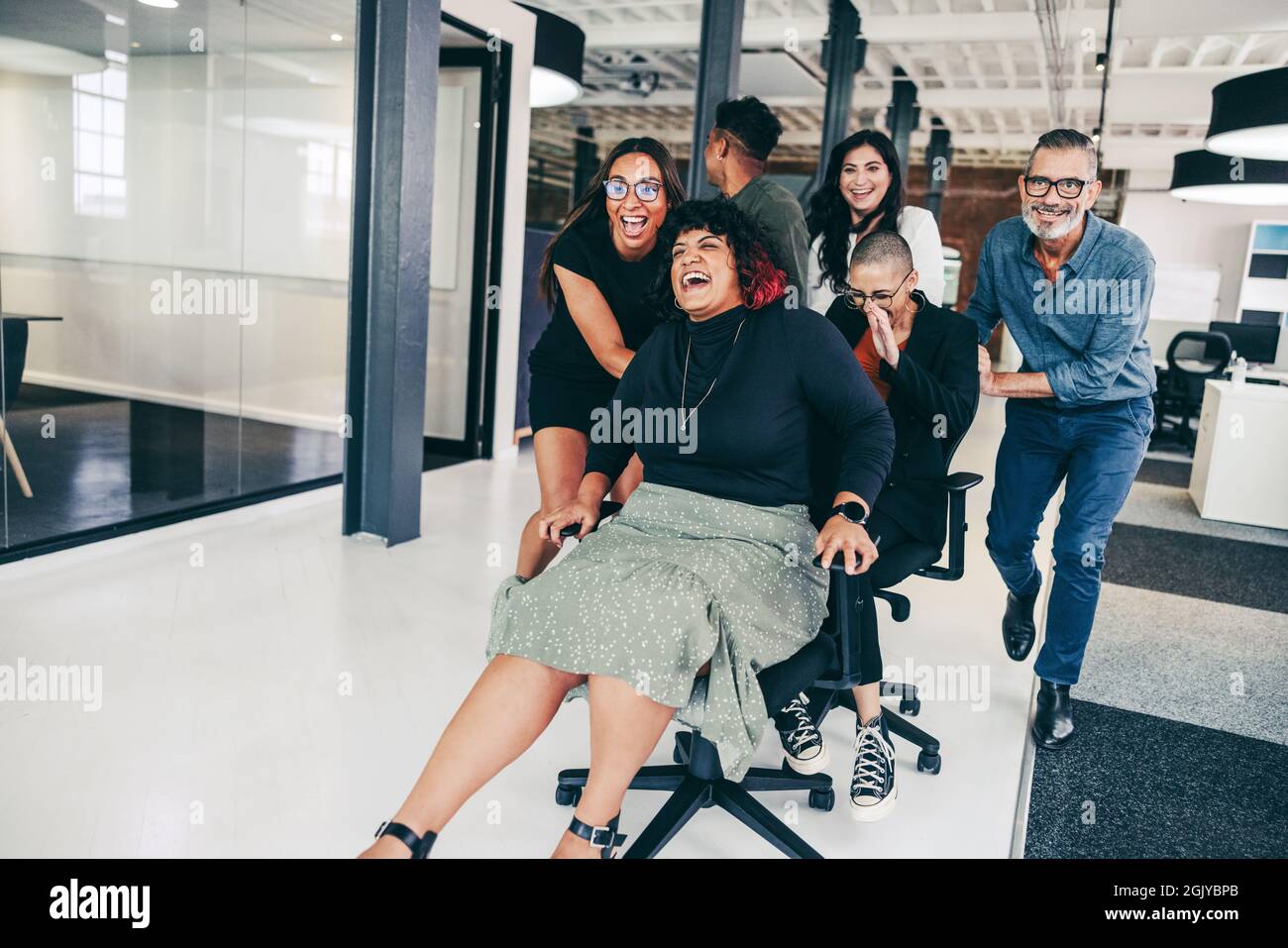 Les hommes d'affaires sans souci s'amusent dans un lieu de travail moderne. Groupe de collègues joyeux se poussant les uns les autres sur des chaises dans un bureau créatif.Happy business Banque D'Images