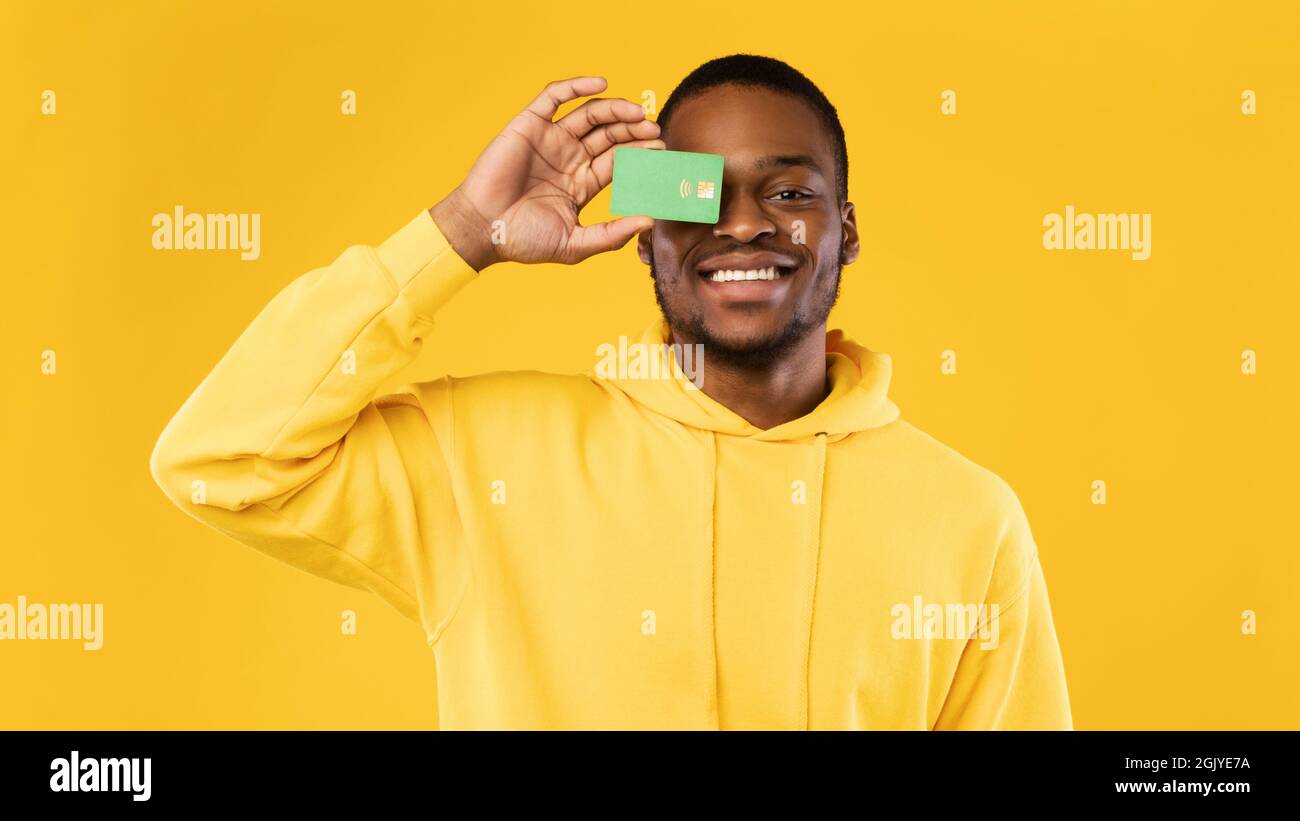 Noir Guy couvrant son oeil avec carte de crédit, fond jaune Banque D'Images