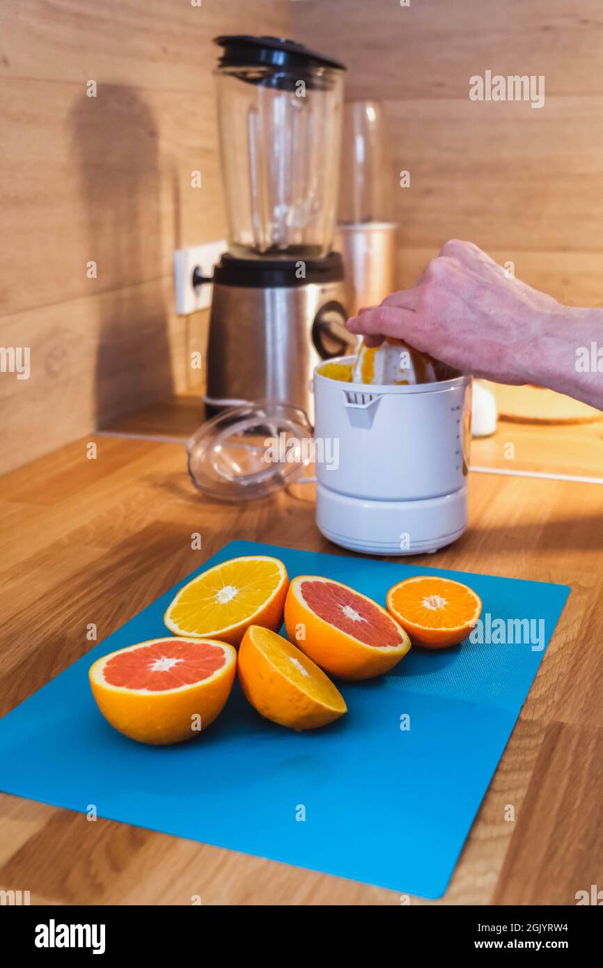 L'homme presse le jus à la centrifugeuse à partir d'oranges rouges et orange  hachées dans la cuisine, en gros plan Photo Stock - Alamy