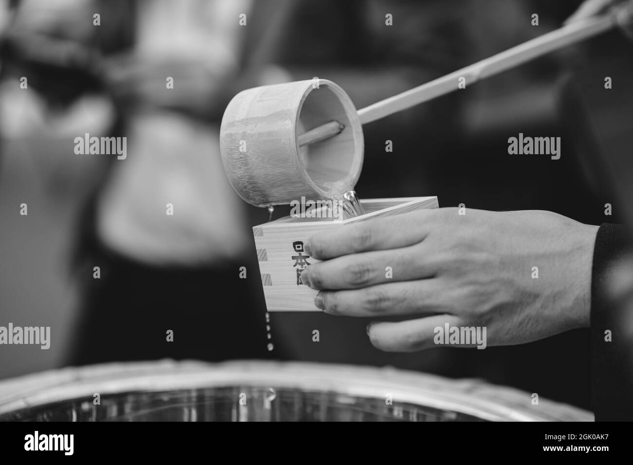 Braila, Roumanie - 26 août 2021: Détails avec les mains d'un homme versant le saké japonais traditionnel dans une tasse en bois. Banque D'Images