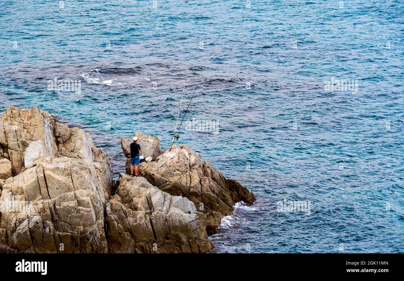 Un pêcheur sur un brise-lames au bord de la mer, avec deux cannes, attendant que le poisson mord. Mise au point sélective. Banque D'Images