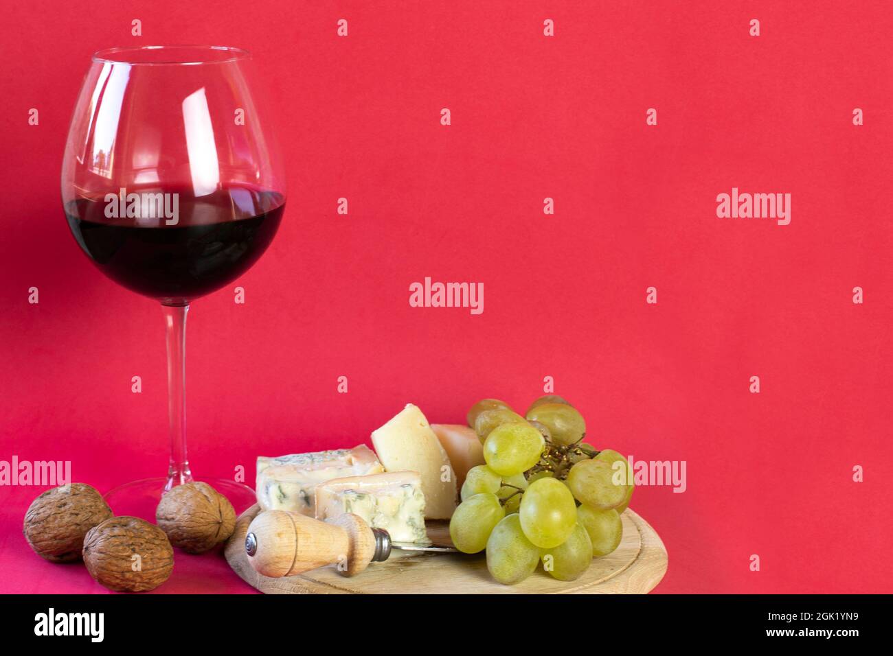 brie, gorgonzola, raisins, noix sur une planche à découper ronde en bois, un verre de vin rouge sur fond rouge Banque D'Images