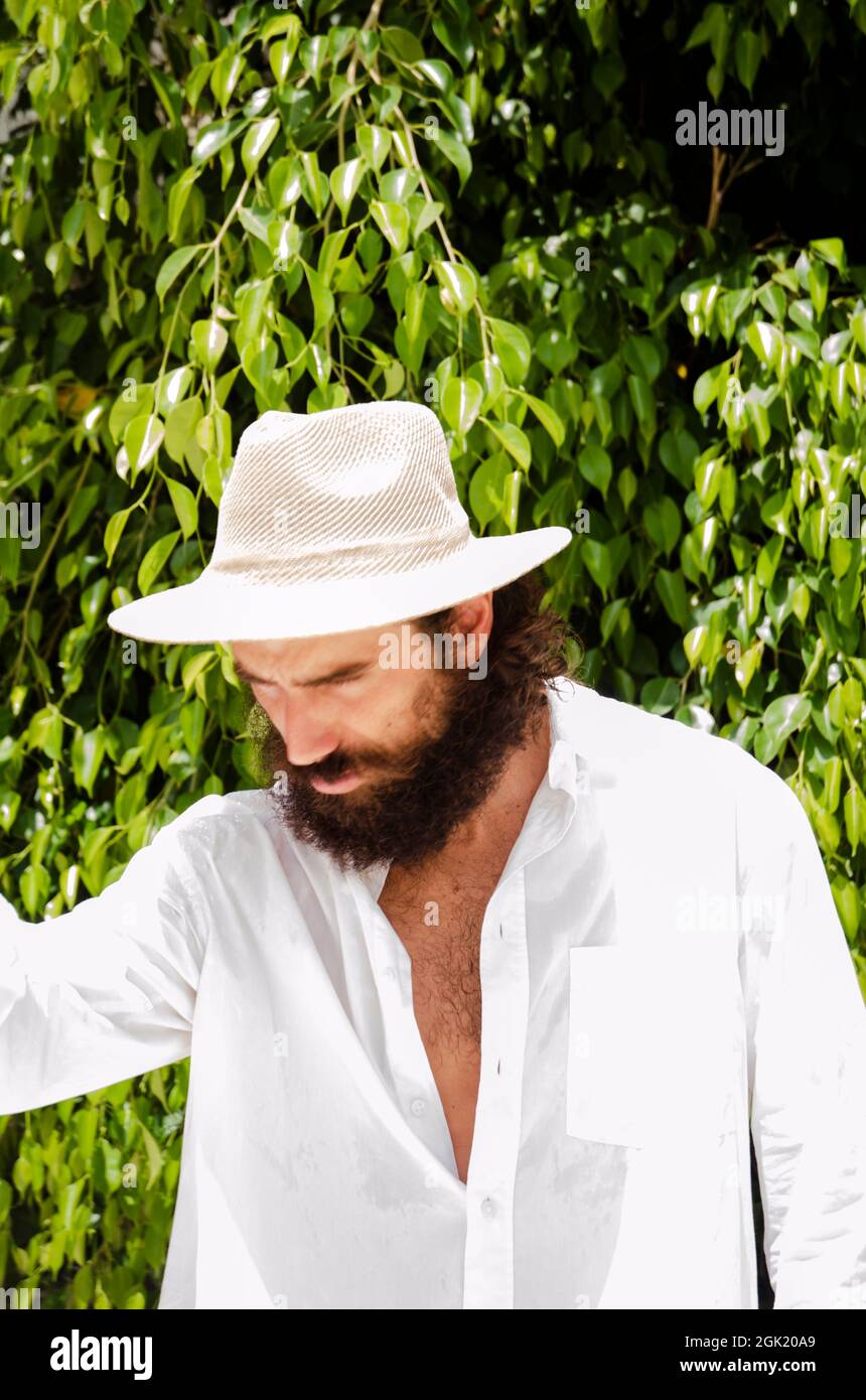 un jeune homme à la barbe et aux cheveux longs porte un chapeau et une  chemise blanche entourée de verdure Photo Stock - Alamy