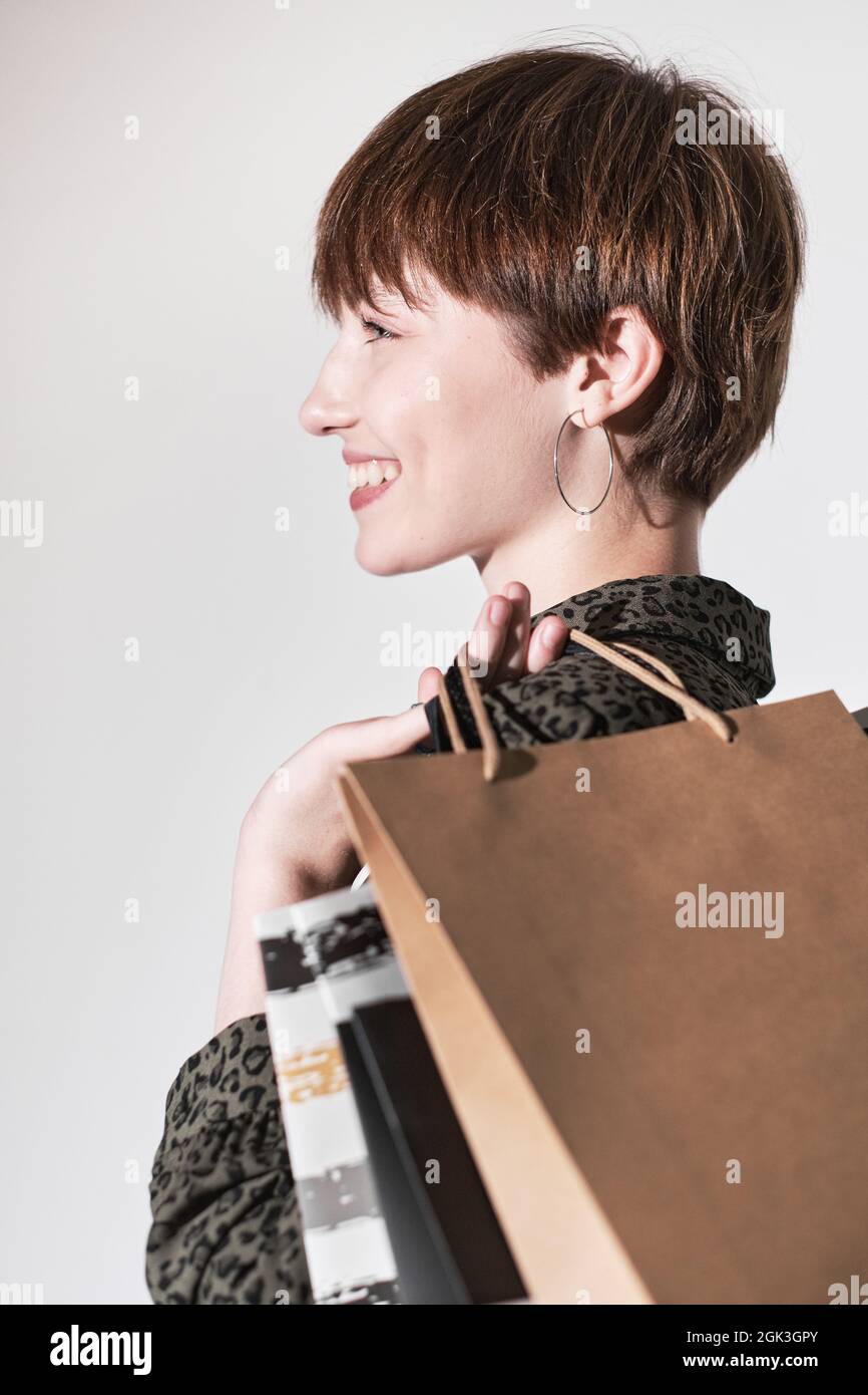 Gros plan de jeune femme aux cheveux courts heureux de ses achats, elle se tenant contre le fond blanc avec des sacs d'achats Banque D'Images