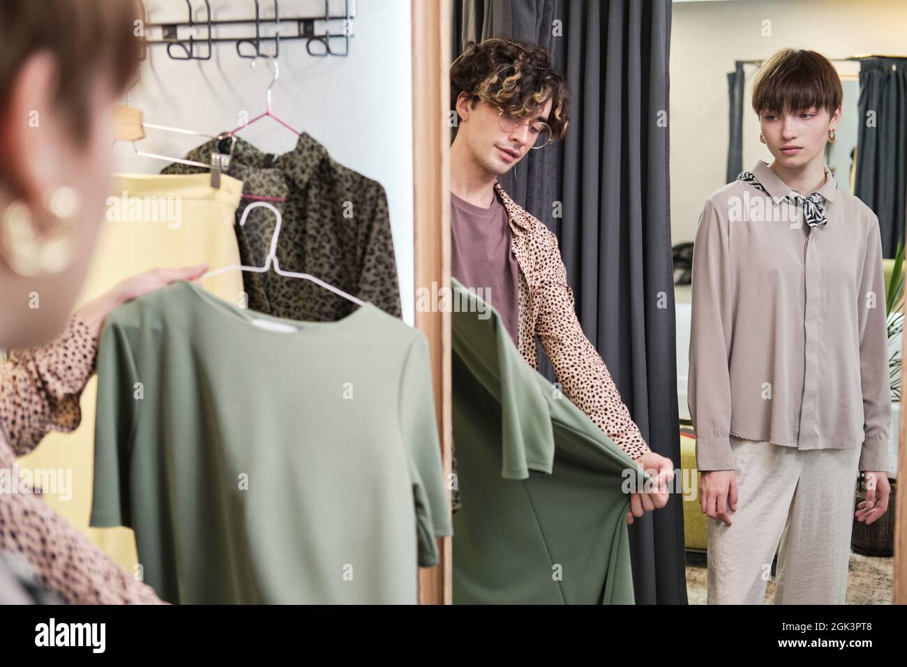 Jeune femme debout dans les cabines d'essayage du magasin alors que la styliste lui suggère de nouveaux vêtements Banque D'Images