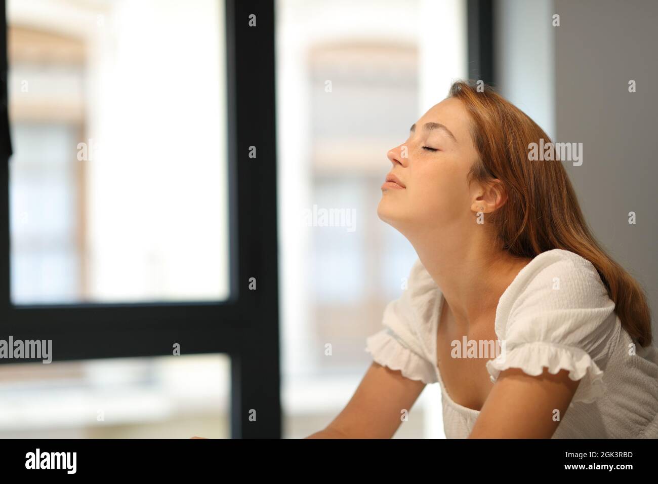 Femme détendue respirant de l'air frais à côté d'une fenêtre à la maison Banque D'Images