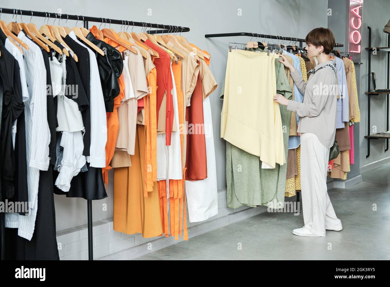 Jeune femme debout près du rack et choisissant de nouveaux vêtements pour  elle-même dans la salle d'exposition Photo Stock - Alamy