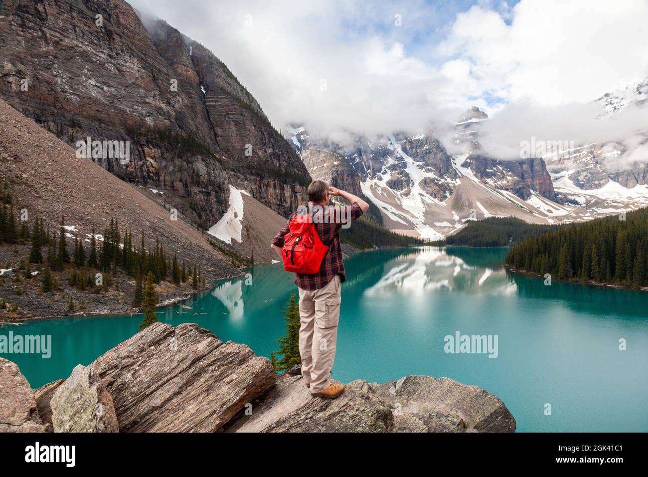 Homme de randonnée avec sac à dos à dos rouge debout sur un rocher surplombant le lac Moraine et regardant les sommets enneigés des montagnes Rocheuses, parc national Banff, A Banque D'Images