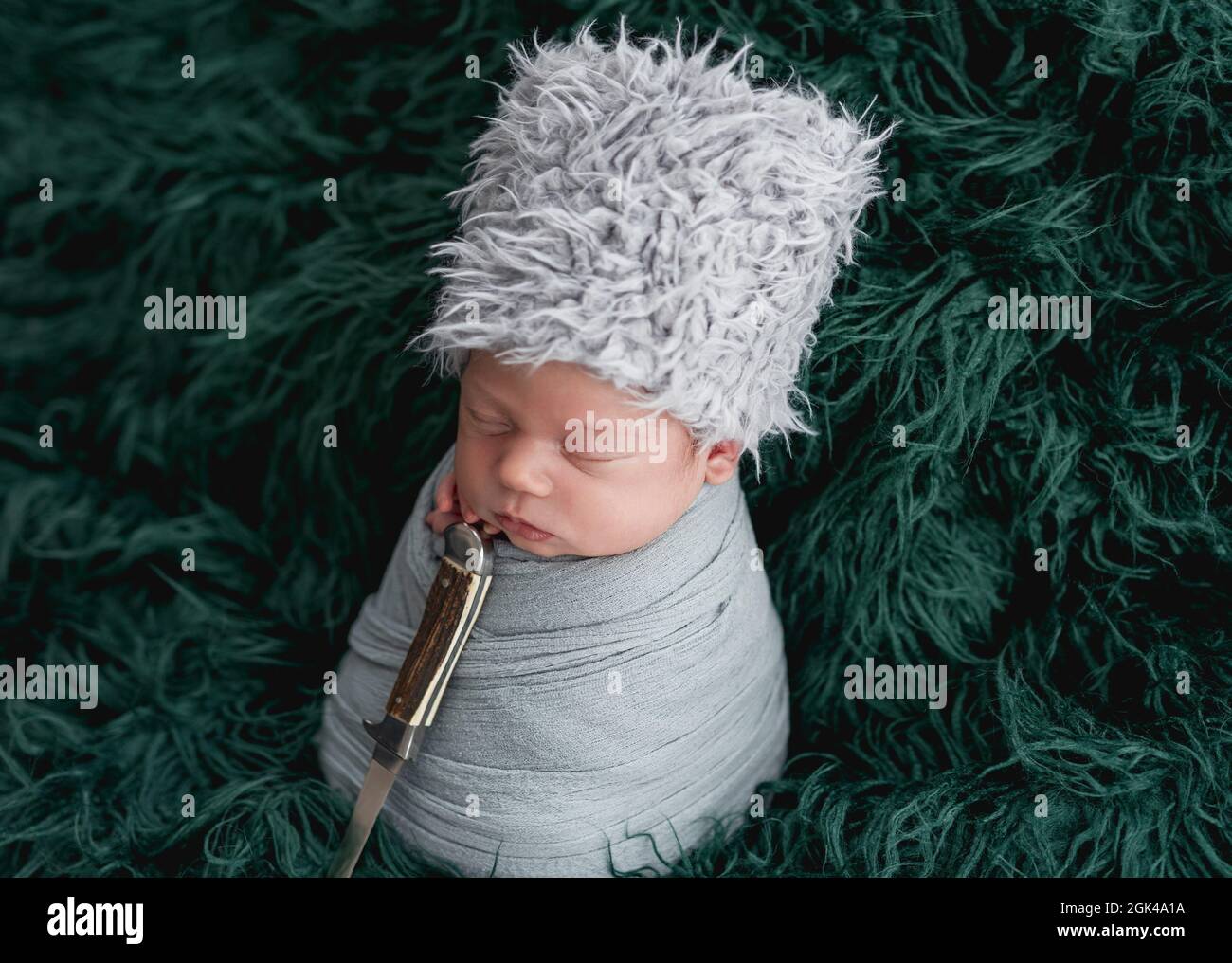 Nouveau-né dans un chapeau ethnique dormant avec un poignard sur fond vert Banque D'Images