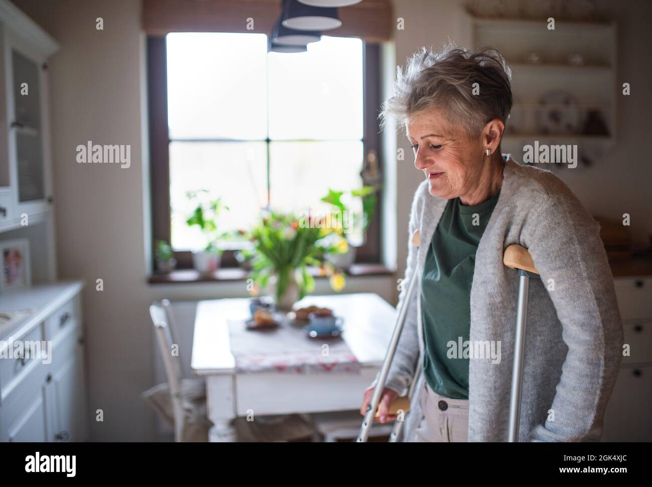 Femme âgée avec des béquilles à l'intérieur à la maison, marchant dans la cuisine. Banque D'Images
