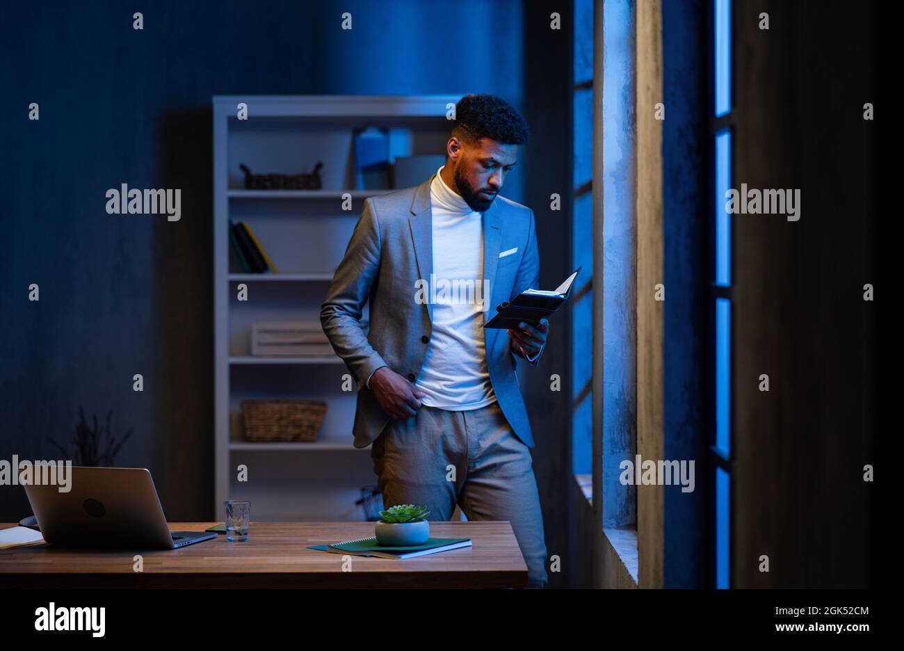 Jeune homme d'affaires afro-américain regardant un journal à l'intérieur dans son bureau la nuit. Banque D'Images