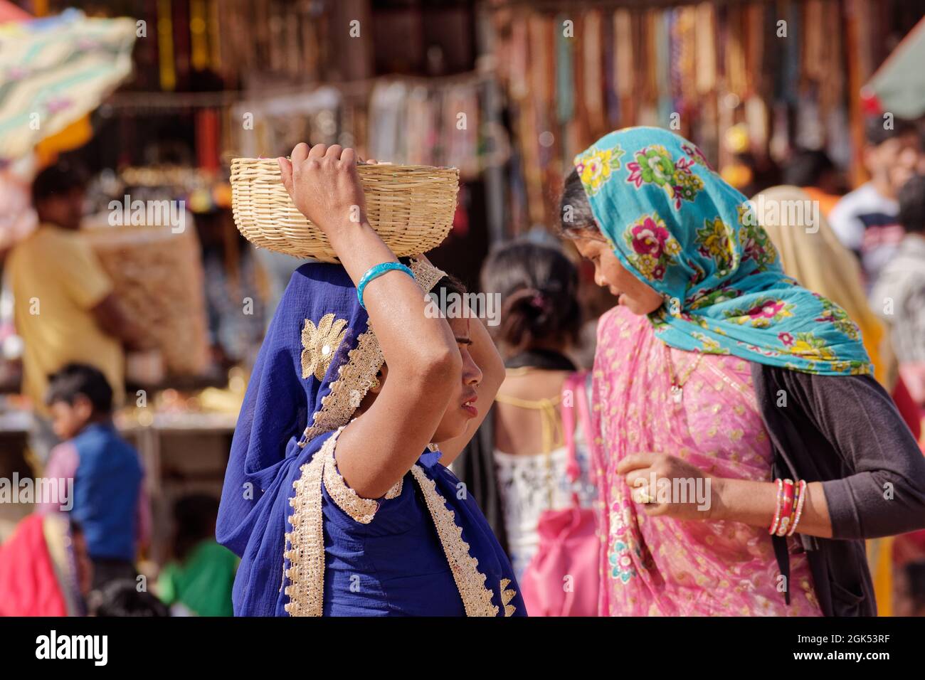 Orcha, Madhya Pradesh, Inde - mars 2019 : une indienne portant un sari bleu portant un panier en osier sur sa tête, sur une place de marché bondée de l'ORC Banque D'Images
