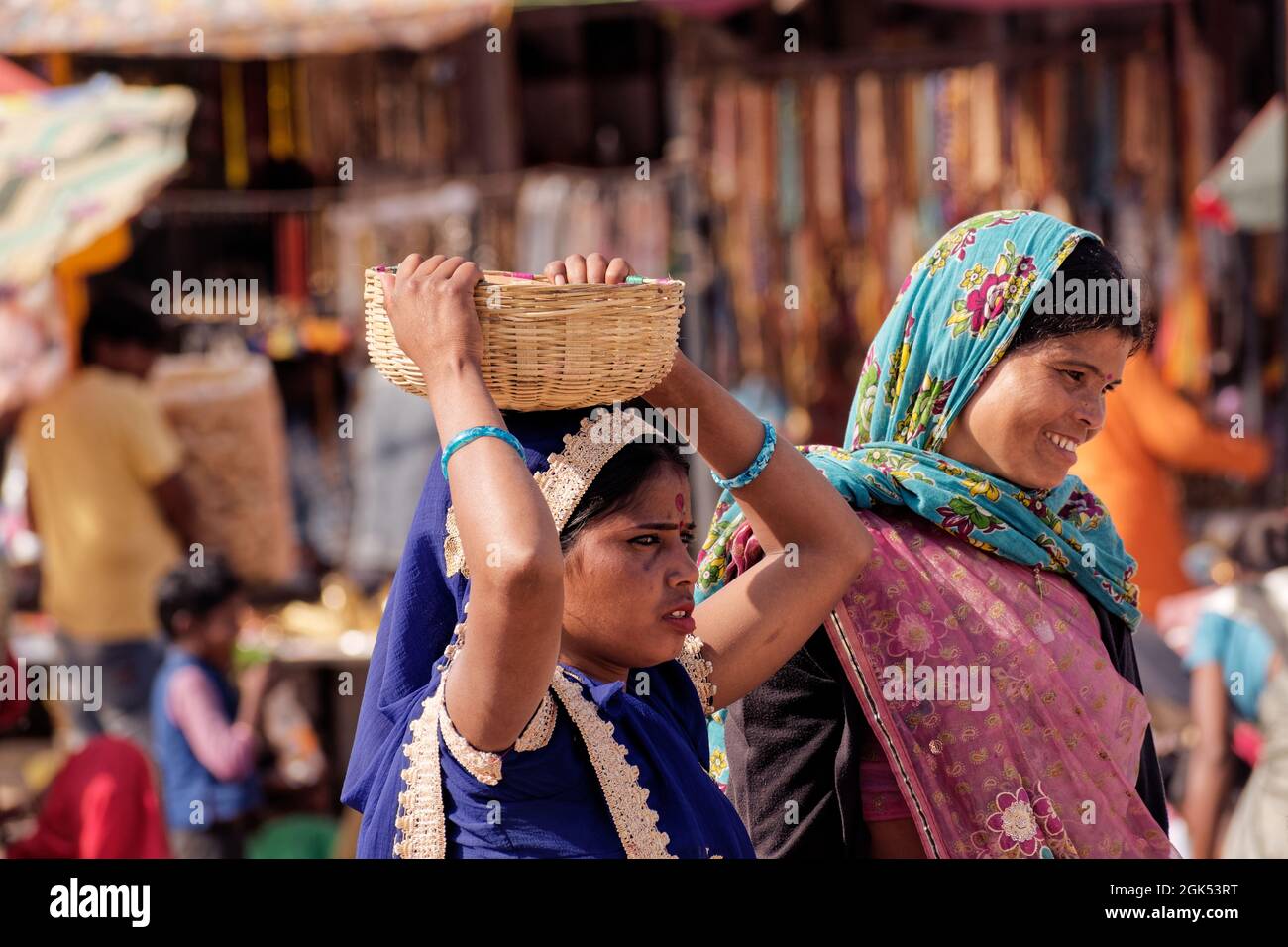 Orcha, Madhya Pradesh, Inde - mars 2019 : une indienne portant un sari bleu portant un panier en osier sur sa tête, sur une place de marché bondée de l'ORC Banque D'Images