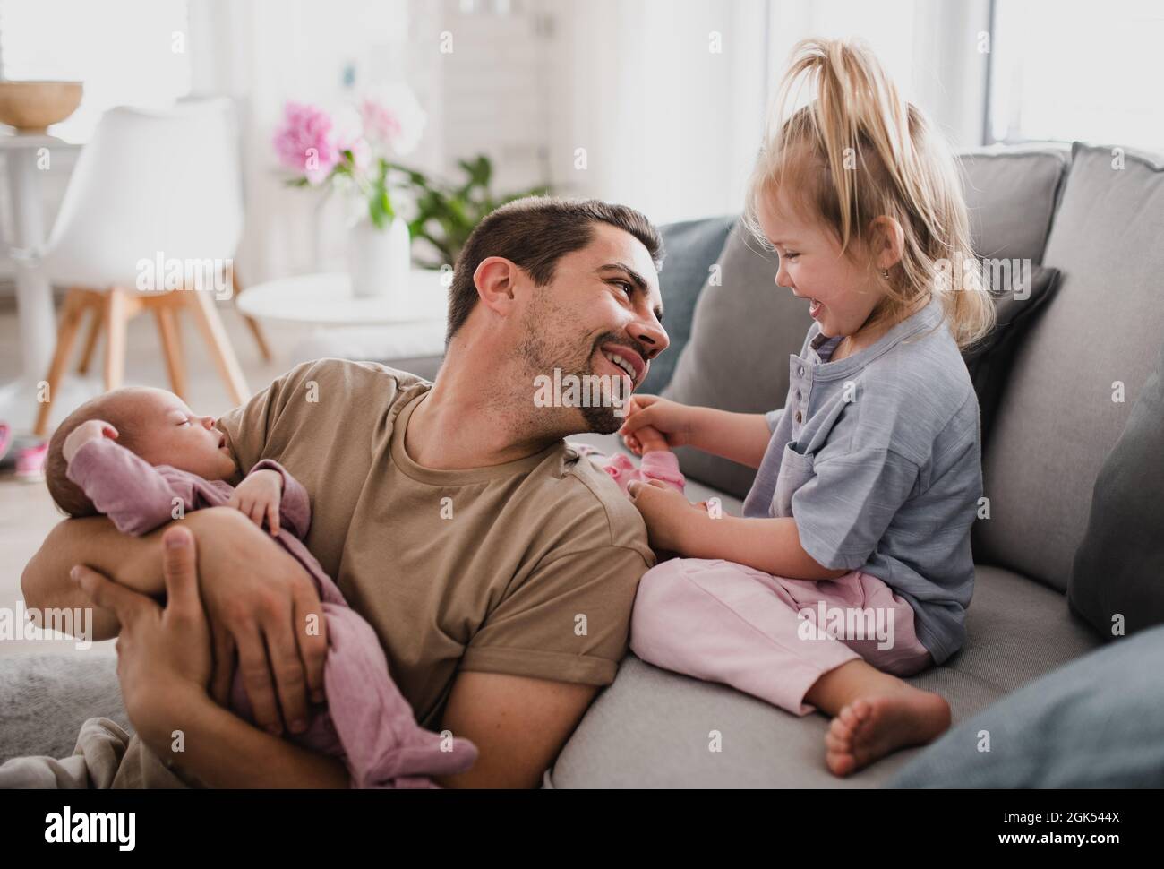 Jeune homme heureux prenant soin de son nouveau-né et petite fille à l'intérieur à la maison, congé de paternité. Banque D'Images