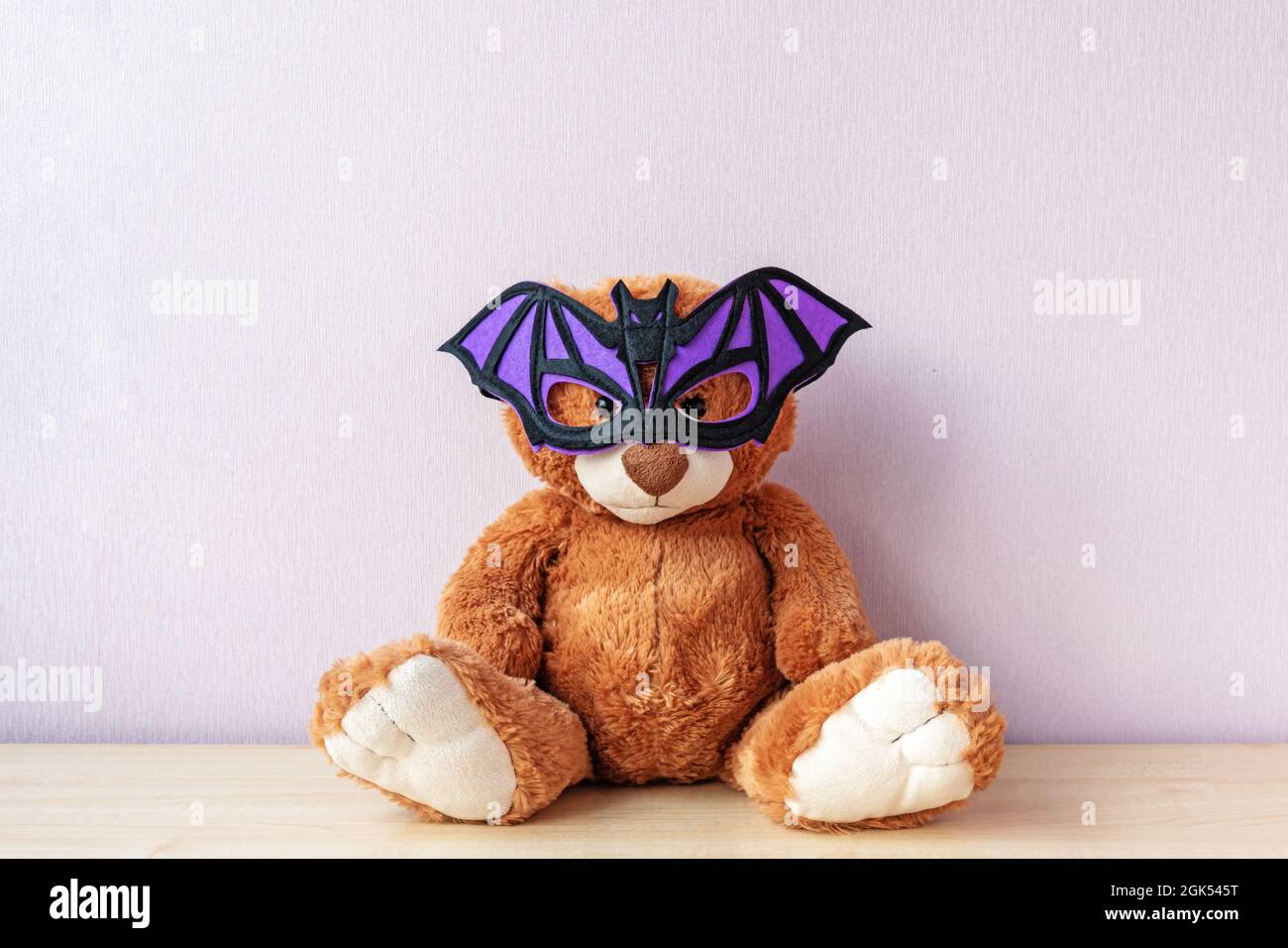 L'ours en peluche avec un masque en forme de chauve-souris est posé sur une table en bois Banque D'Images