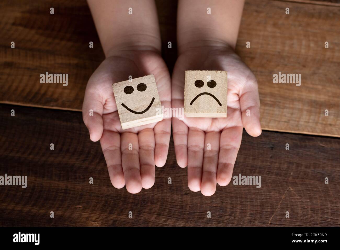 Main d'enfant tenant un cube en bois avec un visage souriant et triste icône. Concept d'émotion, d'expression et de notation Banque D'Images