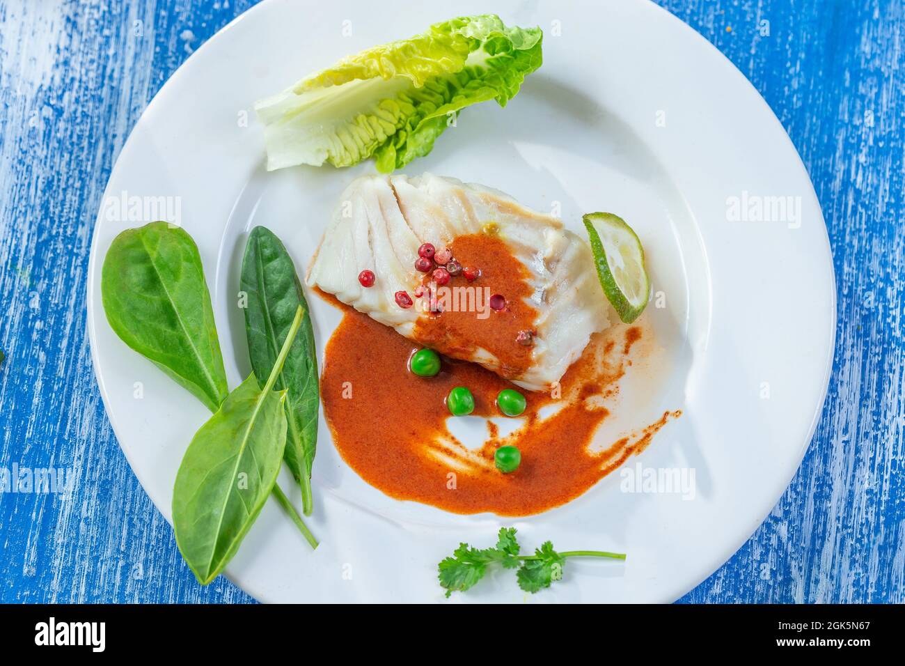 Filet de morue à la vapeur avec sauce paprika et feuilles de salade. Banque D'Images