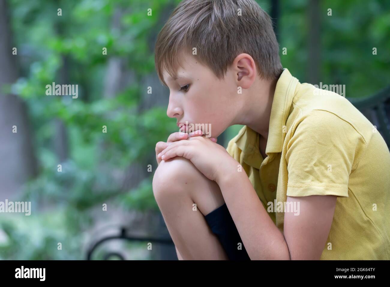 Le triste petit garçon a mis sa tête sur son genou. L'enfant s'ennuie. Banque D'Images