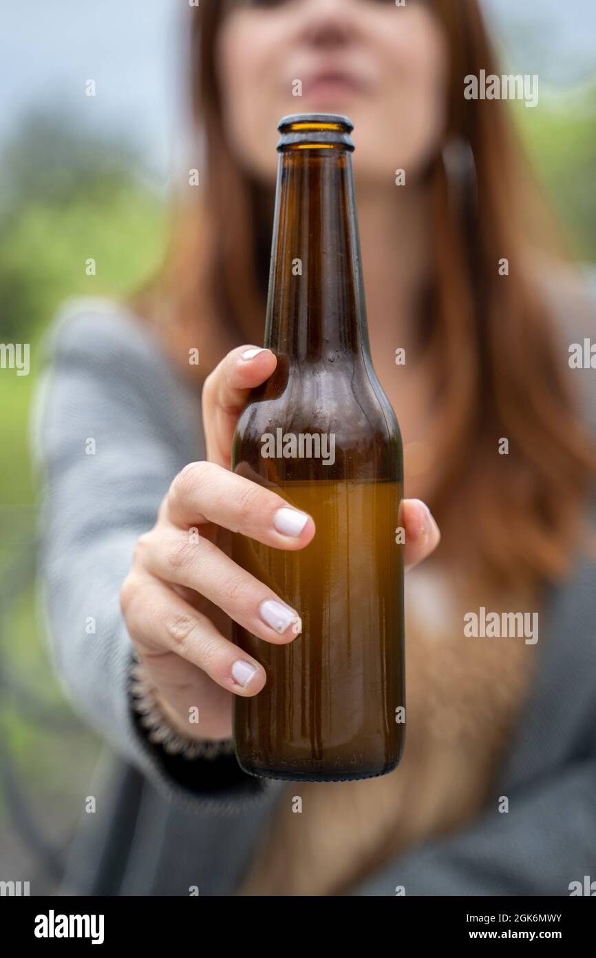 souriante, belle fille face à la caméra montrant de la bière en bouteille. Gros plan avec mise au point sur le visage flou de la bouteille. Arrière-plan naturel. Banque D'Images