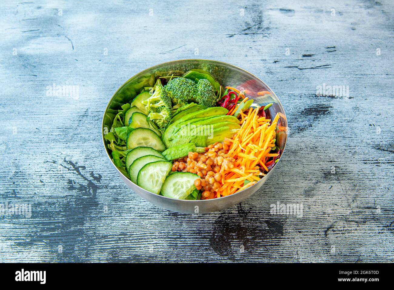 Bol en acier inoxydable rempli de nourriture végétarienne sur table en bois mariné bleu. Banque D'Images