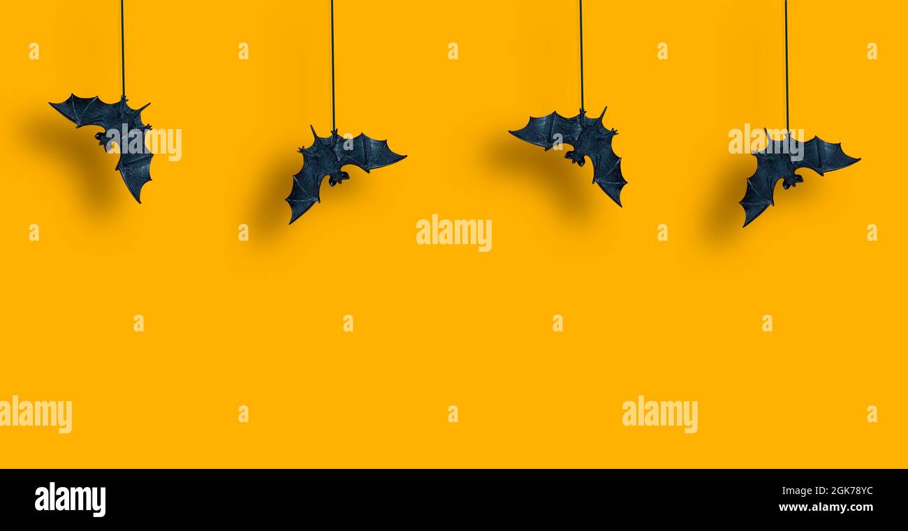 Motif horizontal. Les battes noires en rangée sont suspendues avec des ailes étalées sur fond jaune orange. Hallowen. Copier l'espace Banque D'Images