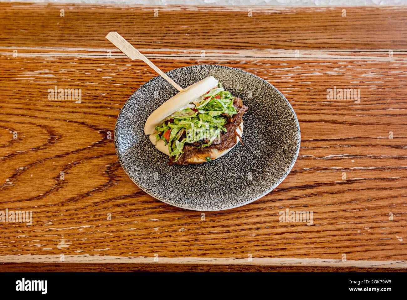 Sandwich asiatique à l'agneau avec sauce teriyaki sur une assiette grise sur une table en bois sombre. Banque D'Images