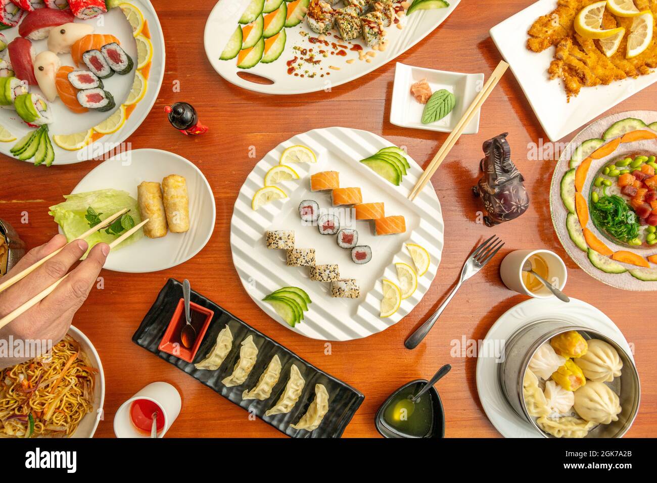 Vue de dessus des plats à sushis, uramaki, algues wakame, wasabi, saumon, thon rouge, main avec baguettes, dim sum et yakisoba assortis Banque D'Images