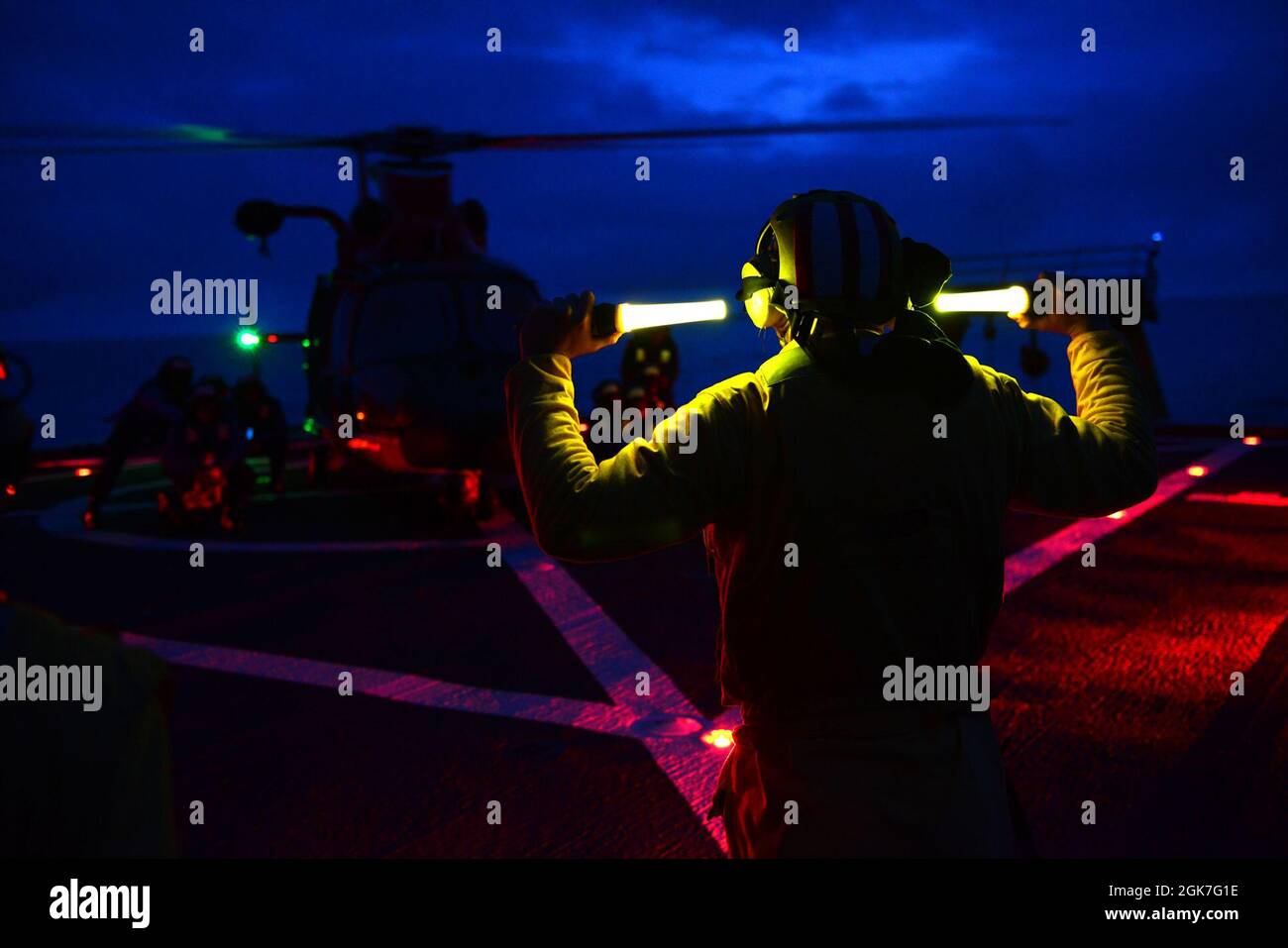 Env. Ryan Dunkle, un membre de l’équipage de la Garde côtière Healy (WAWGB 20), donne des ordres à une équipe d’arrimage lors d’opérations de formation en vol conjoint de nuit avec une équipe de Kodiak de la station aérienne au large de la côte de l’Alaska pendant le déploiement de Healy dans l’Arctique le 25 août 2021. Les agents de signalisation d'atterrissage sont responsables de communiquer avec l'équipage et les membres d'équipage de la découpeuse pendant les opérations de vol. Banque D'Images