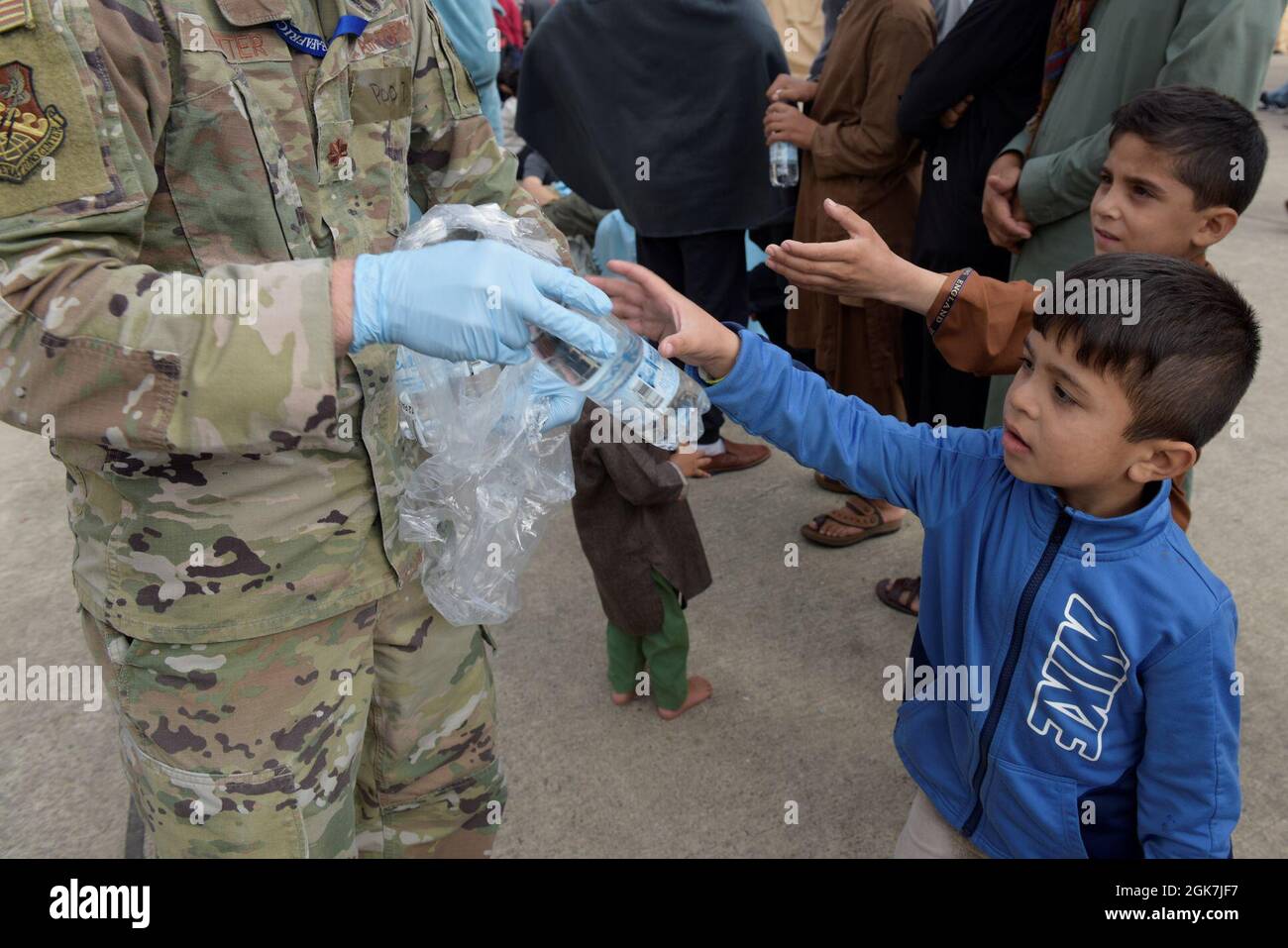 Le Maj. Trek Potter de la US Air Force, 603e chef de la branche des opérations de cyberguerre du Centre des opérations aériennes, donne à un enfant afghan une bouteille d'eau à la base aérienne de Ramstein, en Allemagne, le 26 août 2021. Environ 72,000 bouteilles d'eau et 30,000 repas sont administrés quotidiennement aux évacués à l'appui de l'opération alliés refuge. Banque D'Images