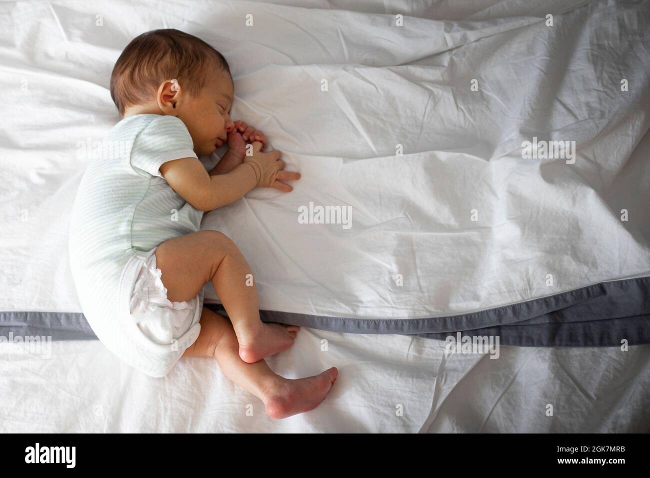 2 mois nouveau-né caucasien, dormant seul dans le lit des parents, allongé sur le côté. Arrière-plan avec espace de copie. Banque D'Images