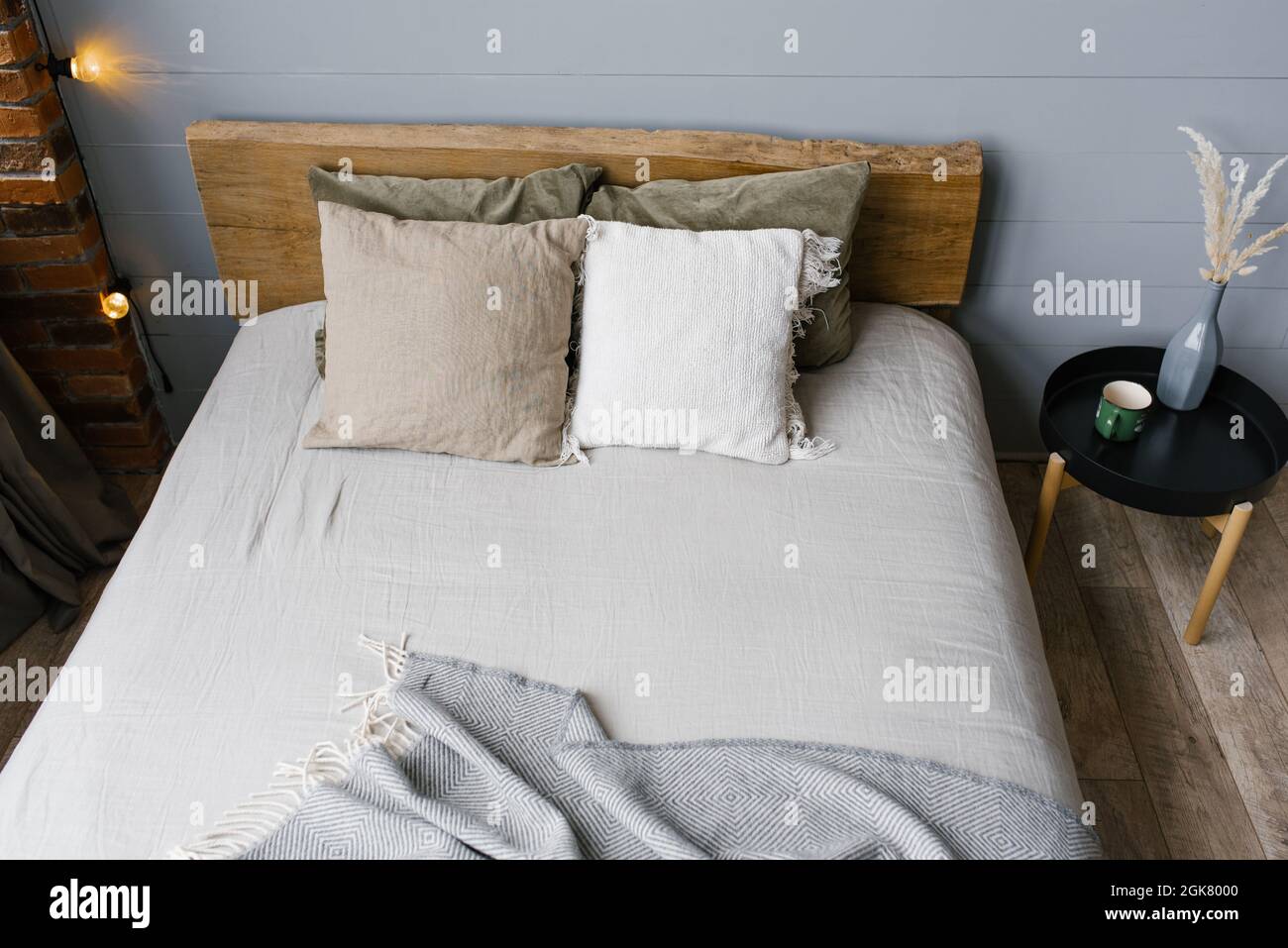 Un vase moderne en céramique blanche avec de l'herbe séchée et une tasse de café ou de thé à côté du lit double. Draps et oreillers gris dans la chambre, scandinave Banque D'Images