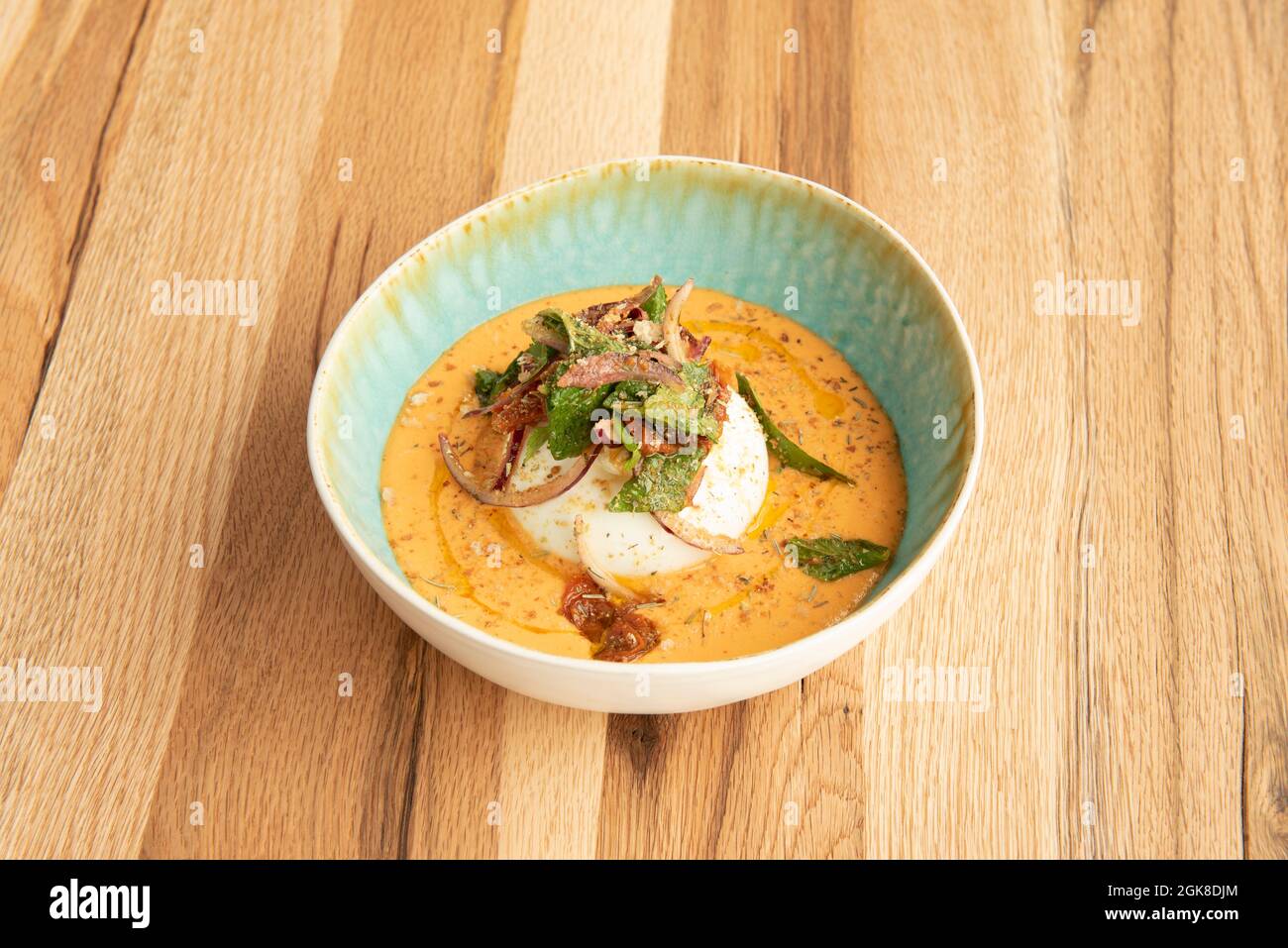 Cuisine fusion de Salmorejo andalou dans un bol bleu avec burrata italien, oignon, tomate séchée et anchois Banque D'Images