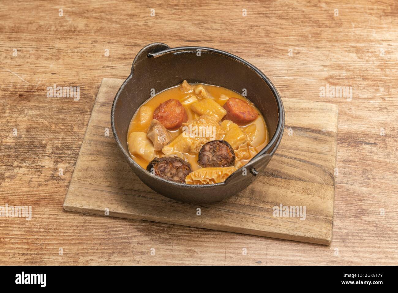 Pot en métal suspendu avec ragoût de tripe de style Madrid avec chorizo et saucisse de sang de riz sur une table en bois Banque D'Images