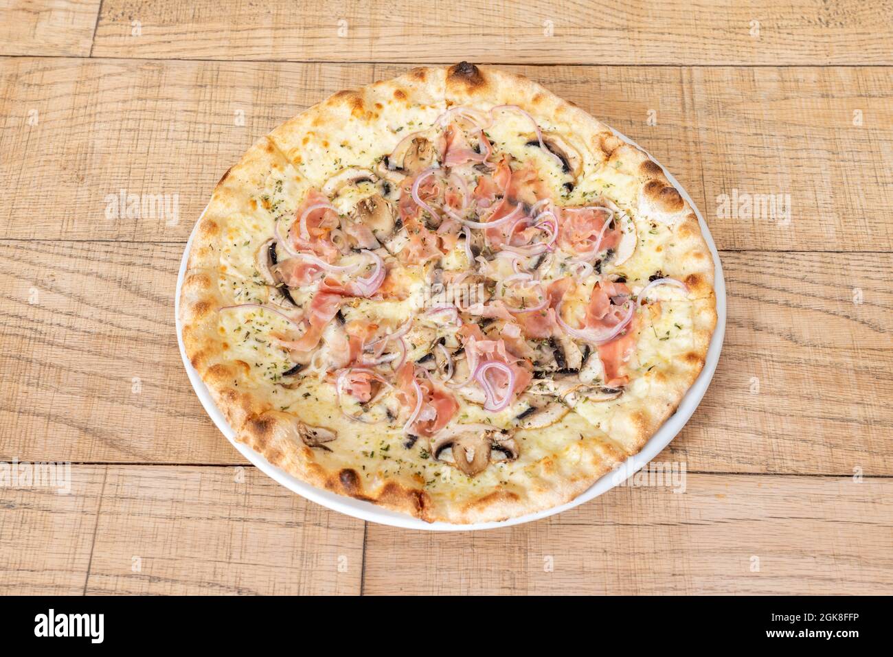 Grande pizza familiale coupée en tranches et cuite avec une recette de carbonara avec oignon rouge, jambon, champignons et fromage fondu Banque D'Images