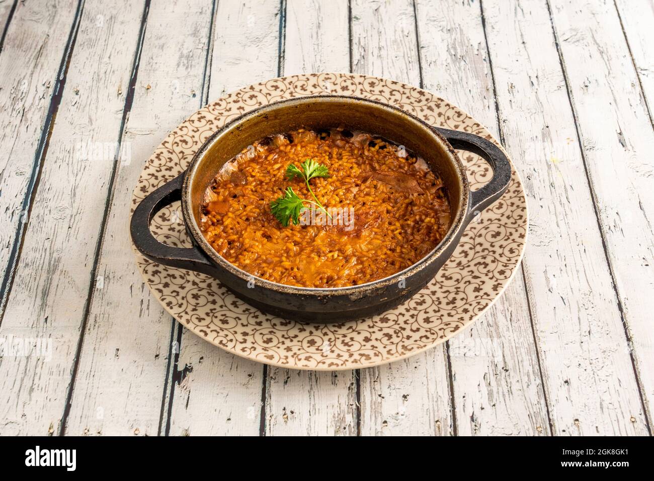 Paella de riz à la seiche servie dans une poêle en métal noir sur une table en bois blanc. Banque D'Images