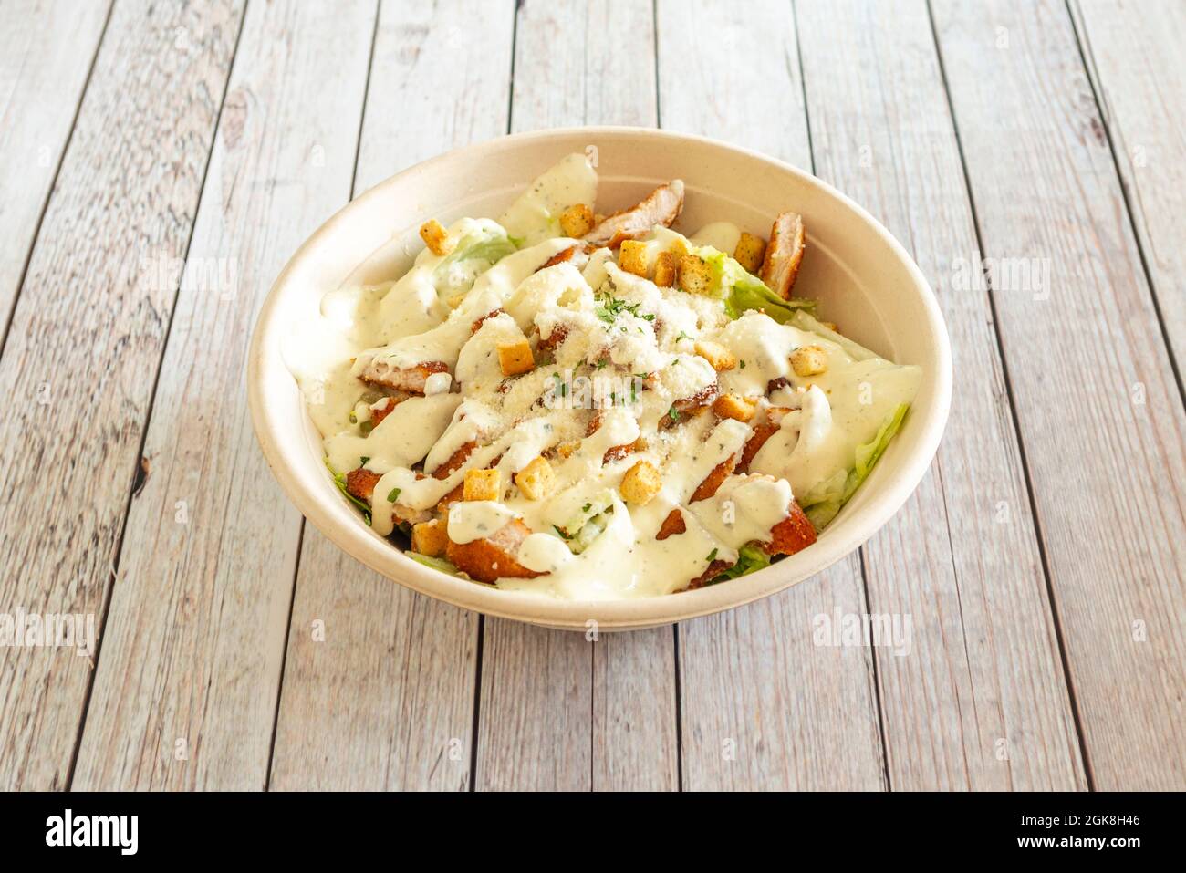 Salade César avec poulet pané et mayonnaise servie dans un bol de livraison à domicile sur une table blanche Banque D'Images