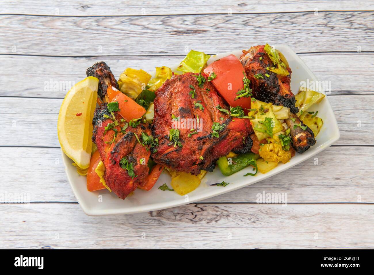 Morceaux de poulet cuits avec une recette tandoori avec beaucoup de persil et de coriandre et garni d'oignon, de poivrons et de citron sur une assiette blanche Banque D'Images