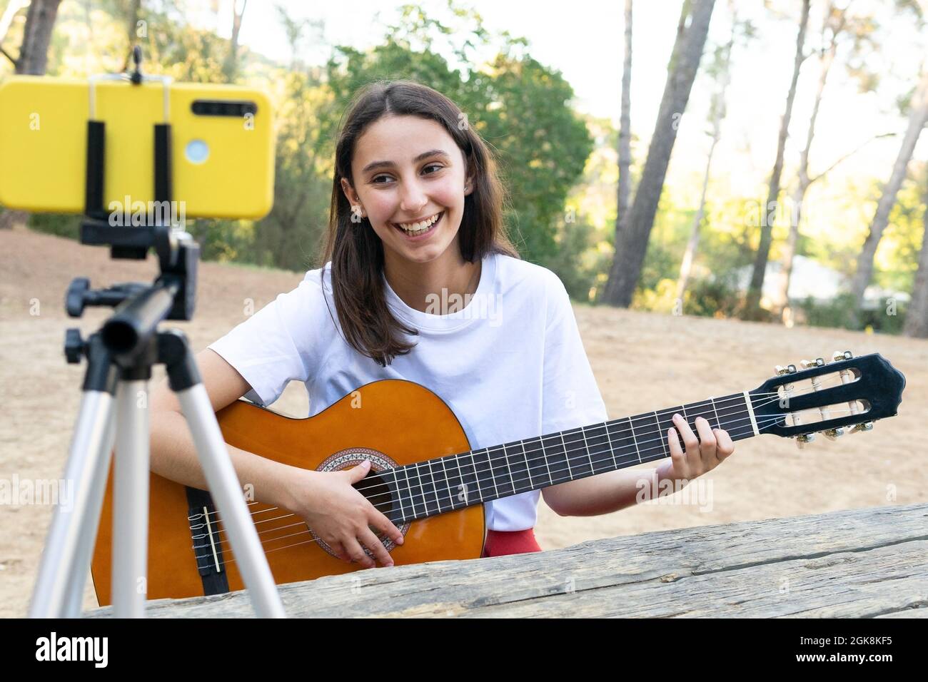 Une jeune femme joyeuse blogueuse jouant de la guitare acoustique tout en  enregistrant de la vidéo sur un téléphone portable sur un trépied dans le  parc Photo Stock - Alamy