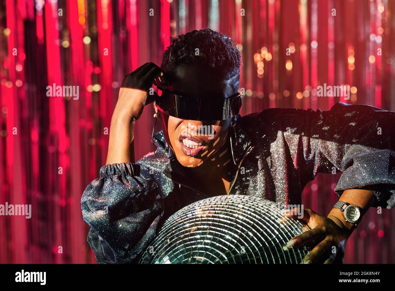 Femme ethnique tendance dans des lunettes cyberpunk et montre-bracelet  touchant le ballon disco dans rayon de lumière Photo Stock - Alamy