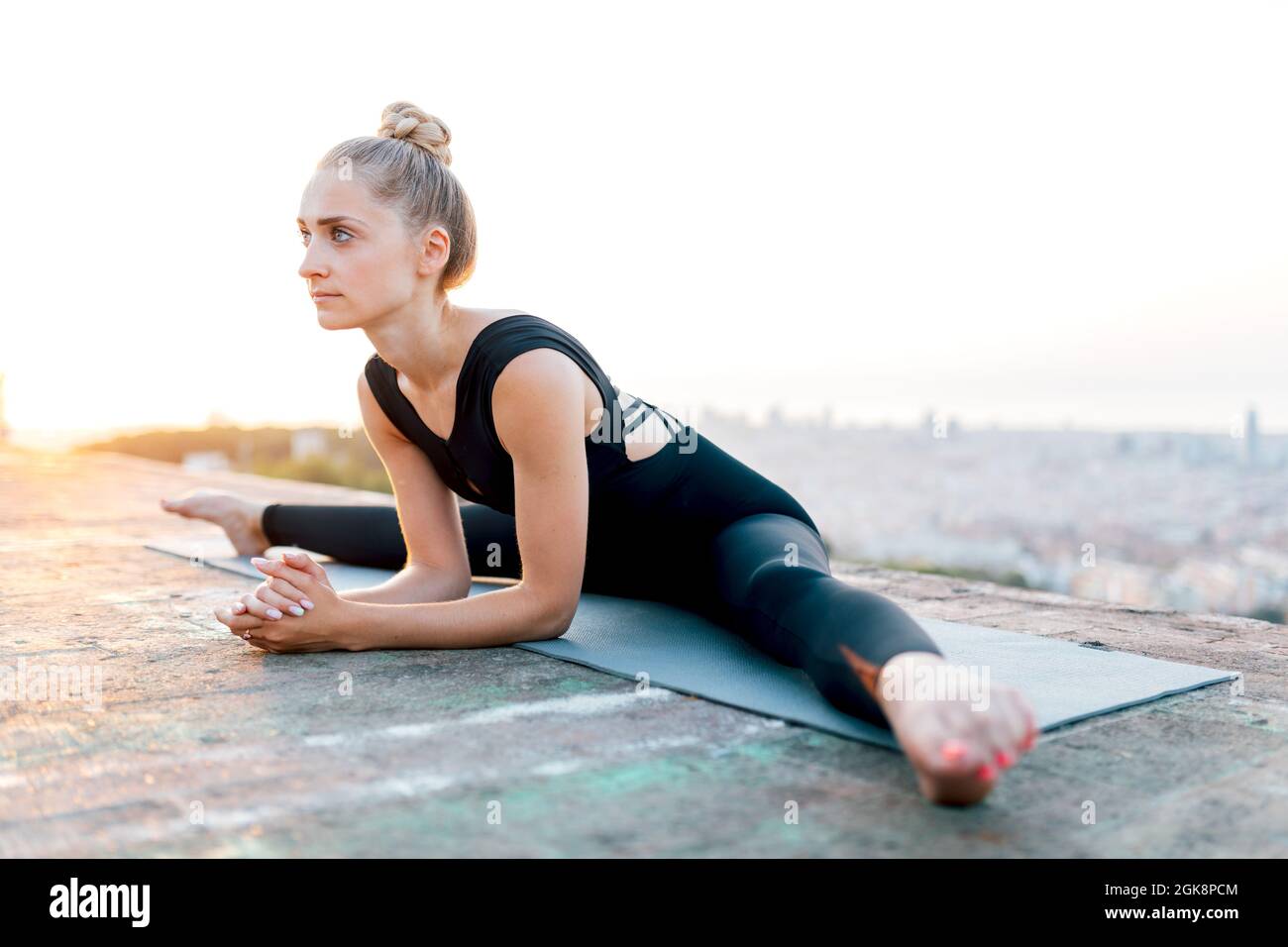 Corps complet de jeunes femmes concentrées pratiquant Upavischta Konasana pendant une séance de yoga en plein air sur le toit au coucher du soleil Banque D'Images