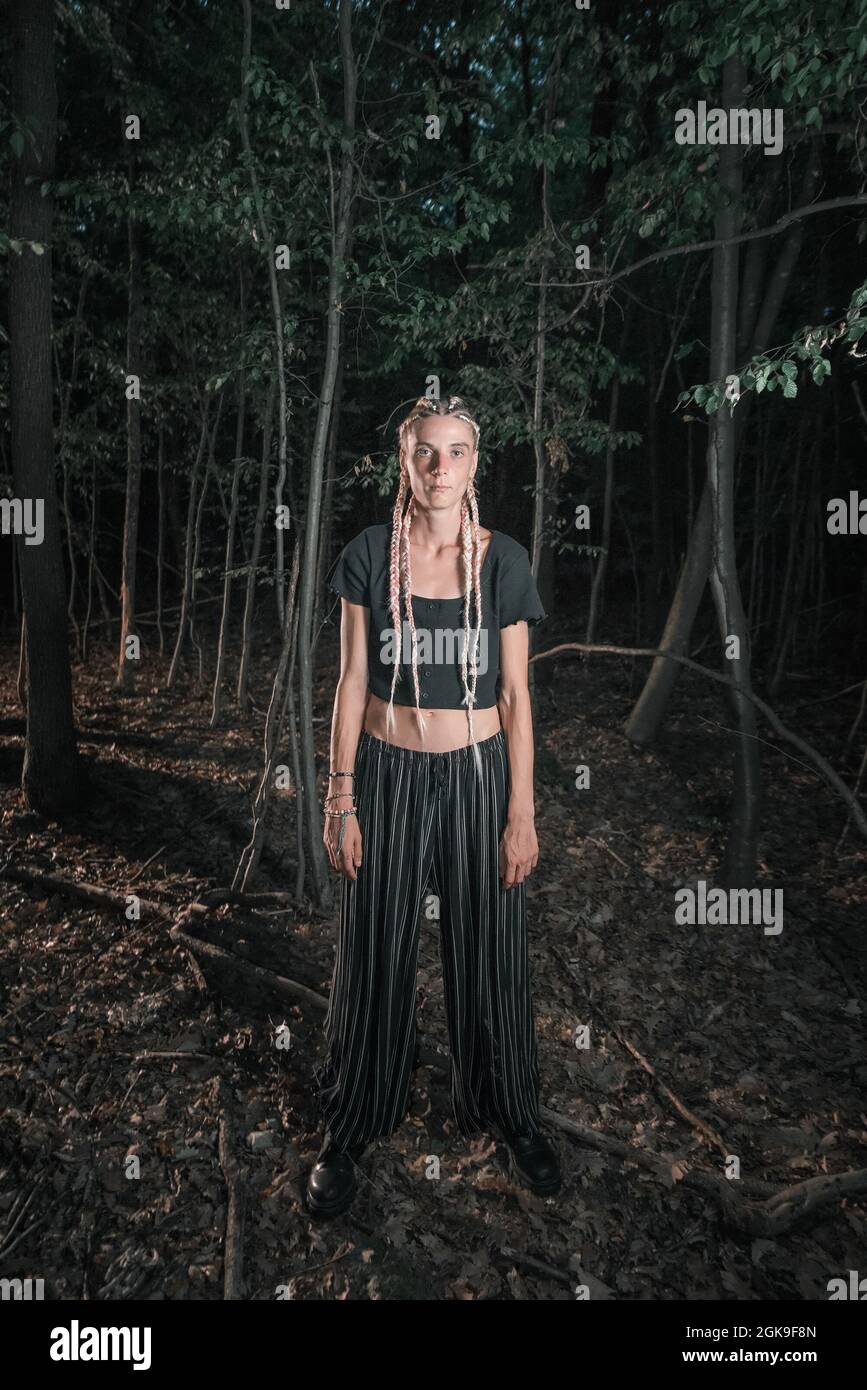 Jeune fillette debout seule dans une forêt sombre Banque D'Images