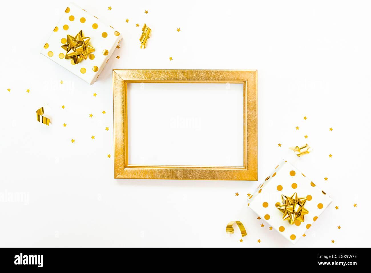 Vue de dessus des boîtes-cadeaux en pointillés dorés et du cadre vide doré sur fond blanc. Espace de copie, maquette. Banque D'Images