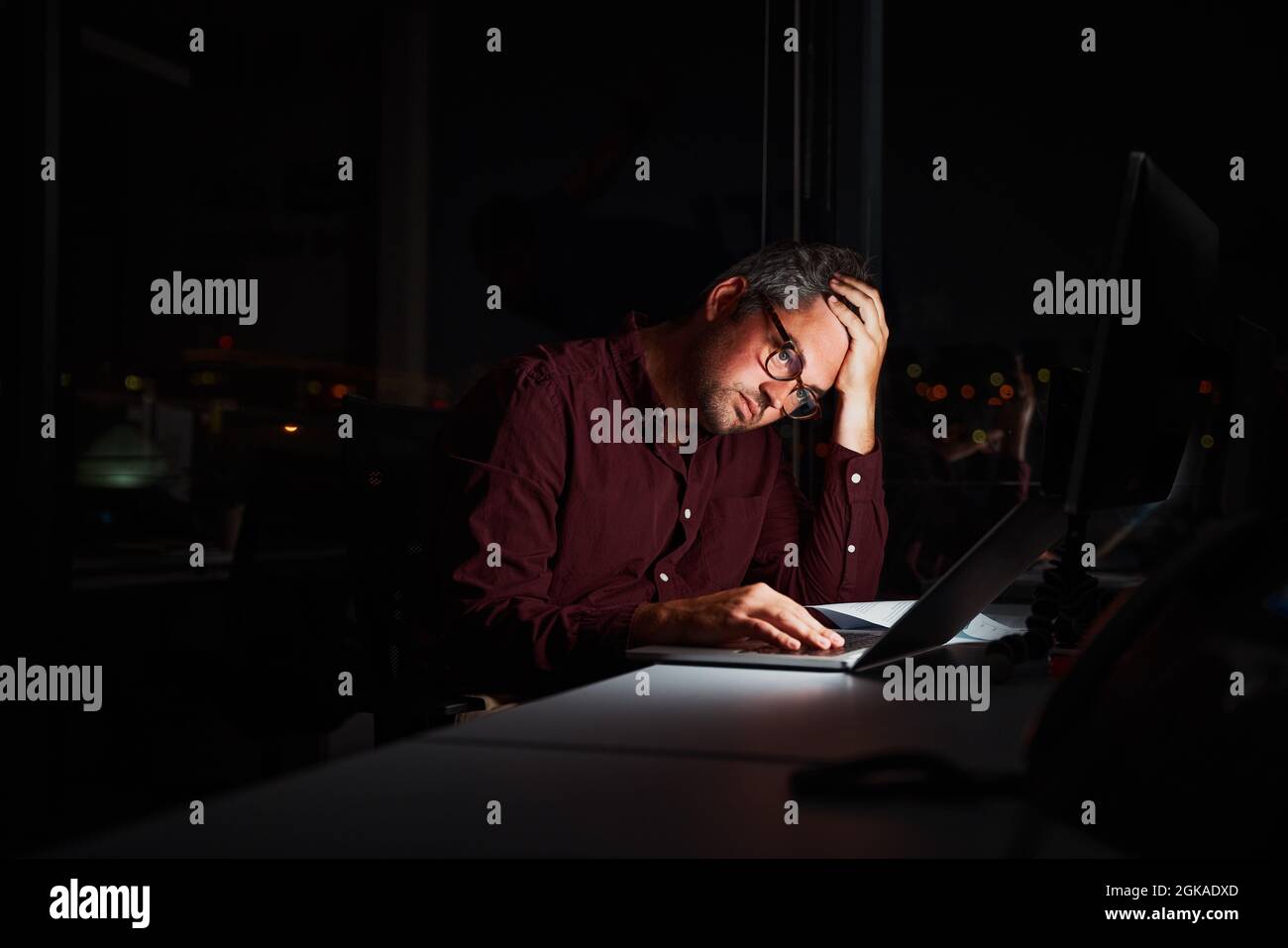 Homme d'affaires fatigué et inquiet au bureau tenant la tête sur les mains après avoir travaillé tard dans la nuit sur un ordinateur portable Banque D'Images