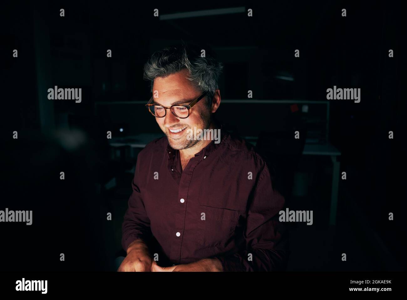 Un homme d'âge moyen souriant qui travaille tard dans le bureau Banque D'Images