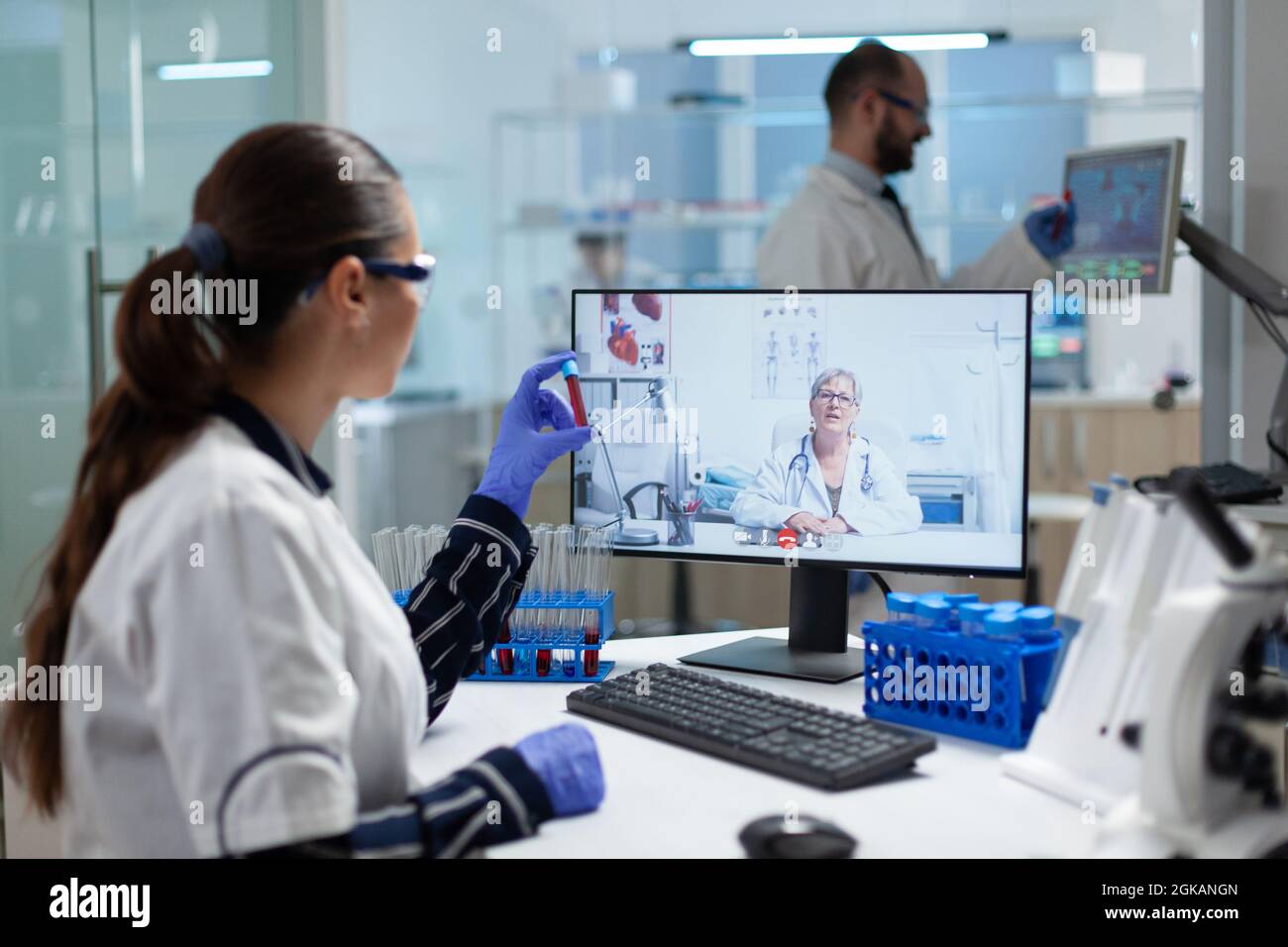 Biologiste chercheuse femme tenant le tube à sang dans les mains discutant d'un vaccin médical avec le médecin chimiste pendant la téléconférence vidéo en ligne dans le laboratoire de l'hôpital. Conférence virtuelle scientifique Banque D'Images