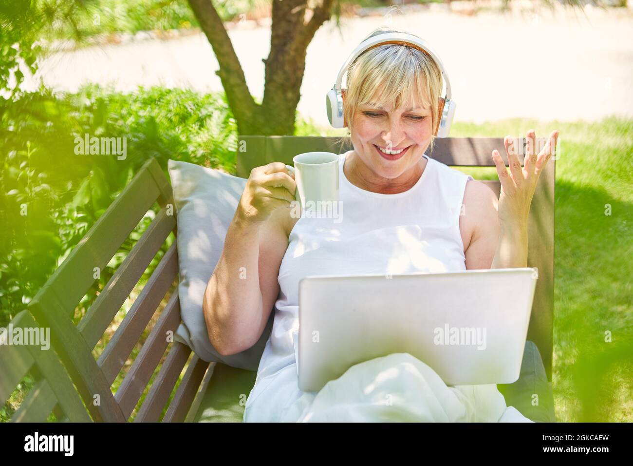 Femme pigiste souriante buvant une tasse de café à l'ordinateur en été dans le jardin Banque D'Images